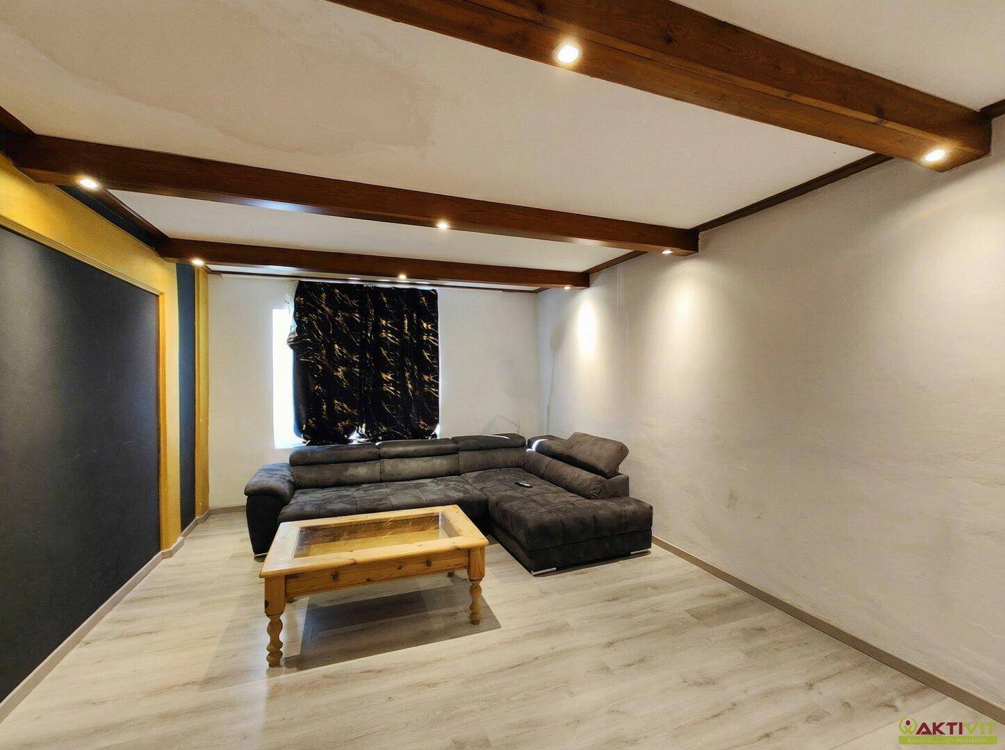 Geräumiges Wohnzimmer mit Holzbalkendecke, Ecksofa und Laminatboden.