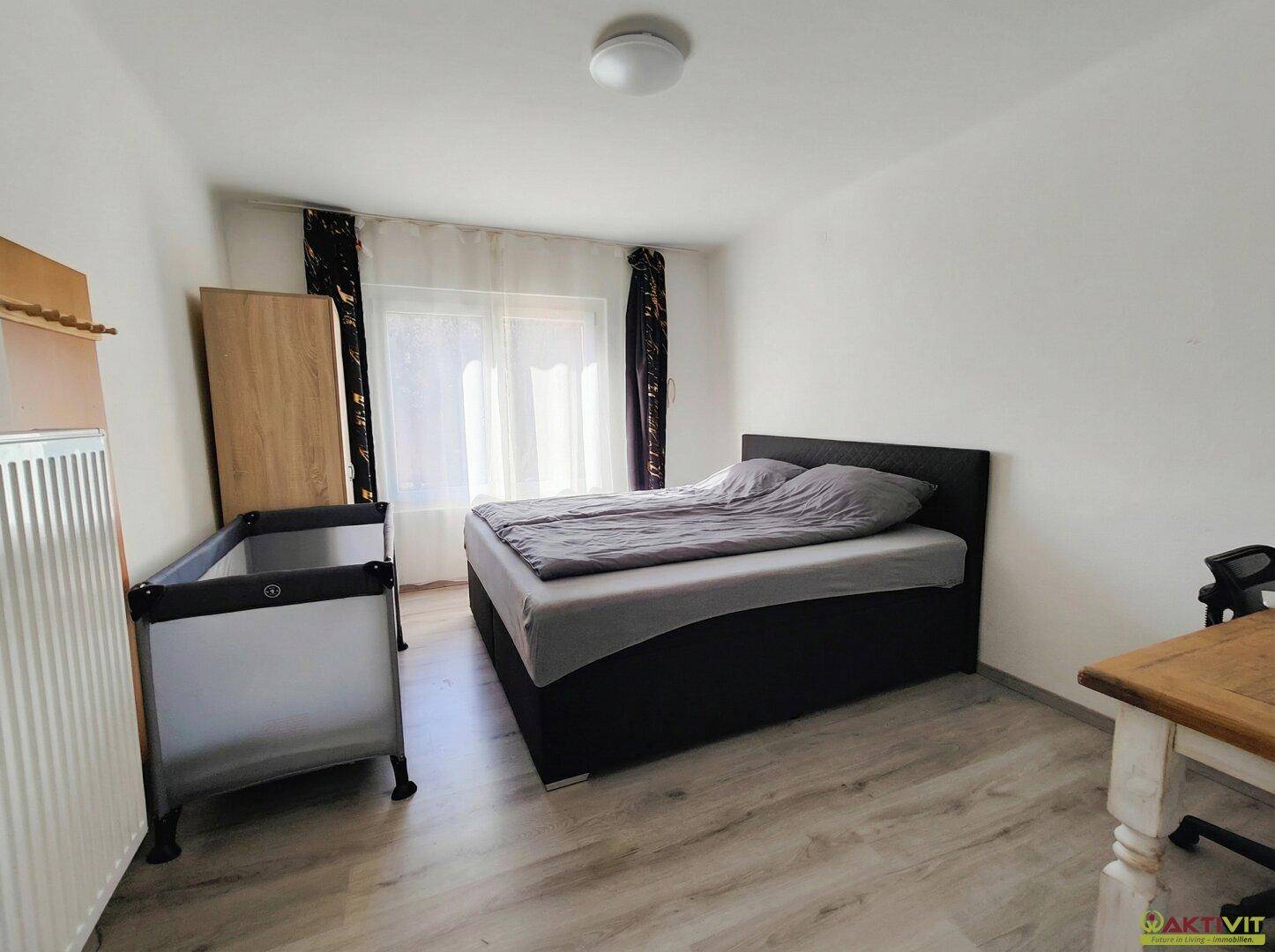 Helles Schlafzimmer mit Doppelbett, Kinderbett und Laminatboden.