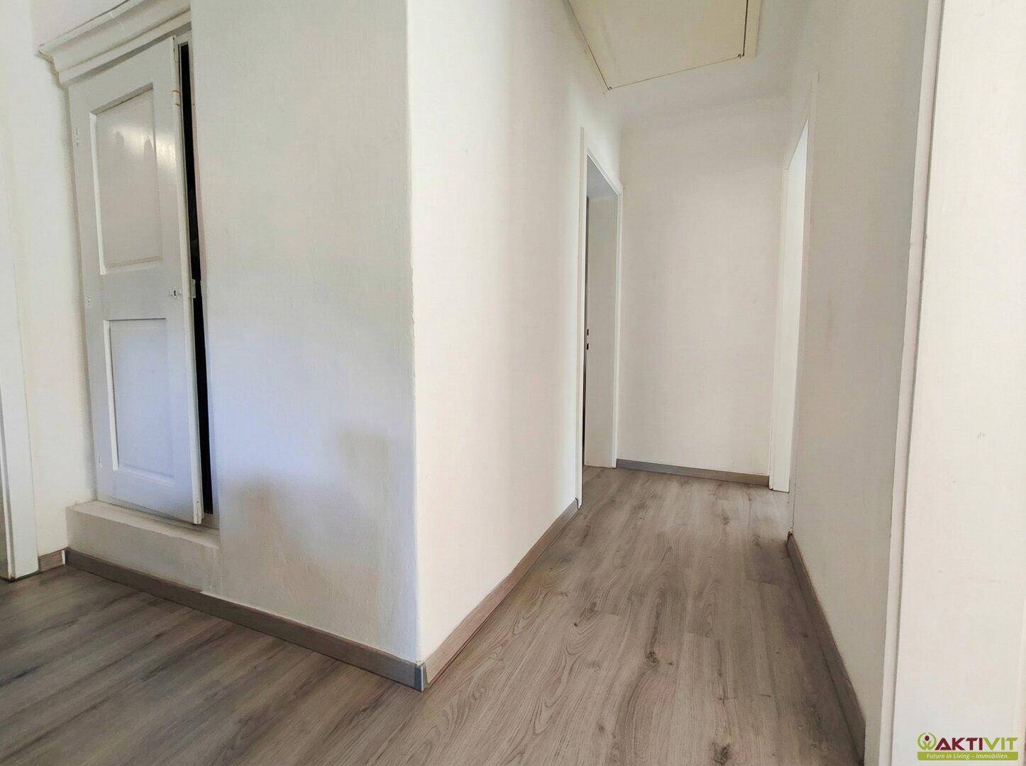 Schmaler Flur mit Laminatboden und weißen Wänden, der zu weiteren Räumen führt.