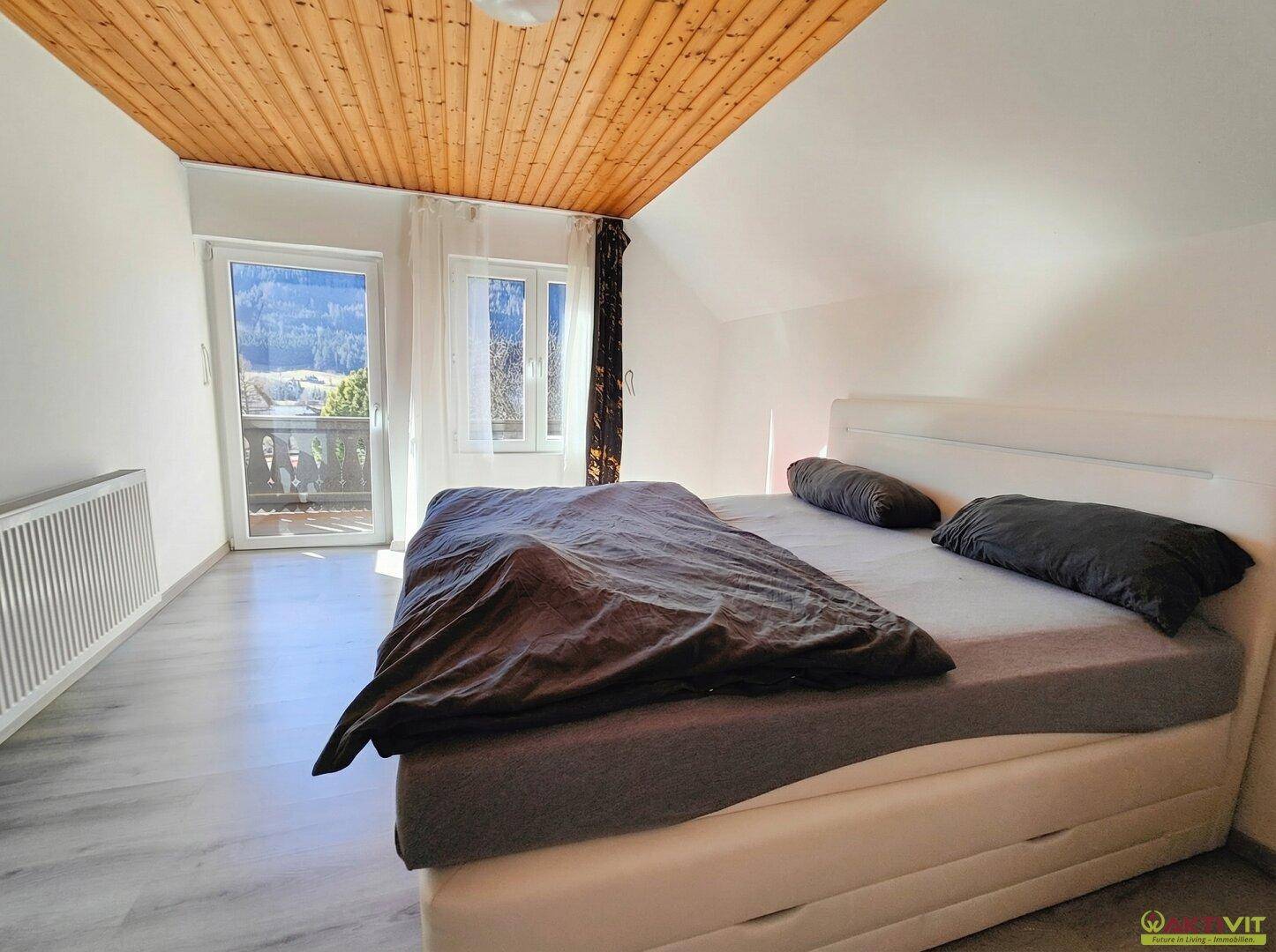 Gemütliches Schlafzimmer mit Holzbalkendecke, Balkonzugang und Bergblick.