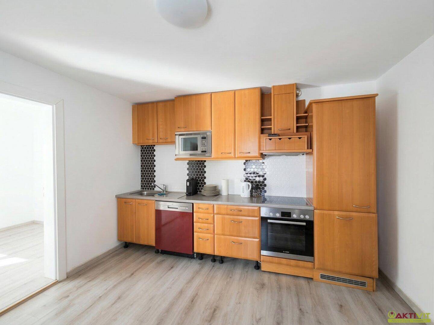 Kompakte Küche mit Holzschränken, integrierten Geräten und Laminatboden.