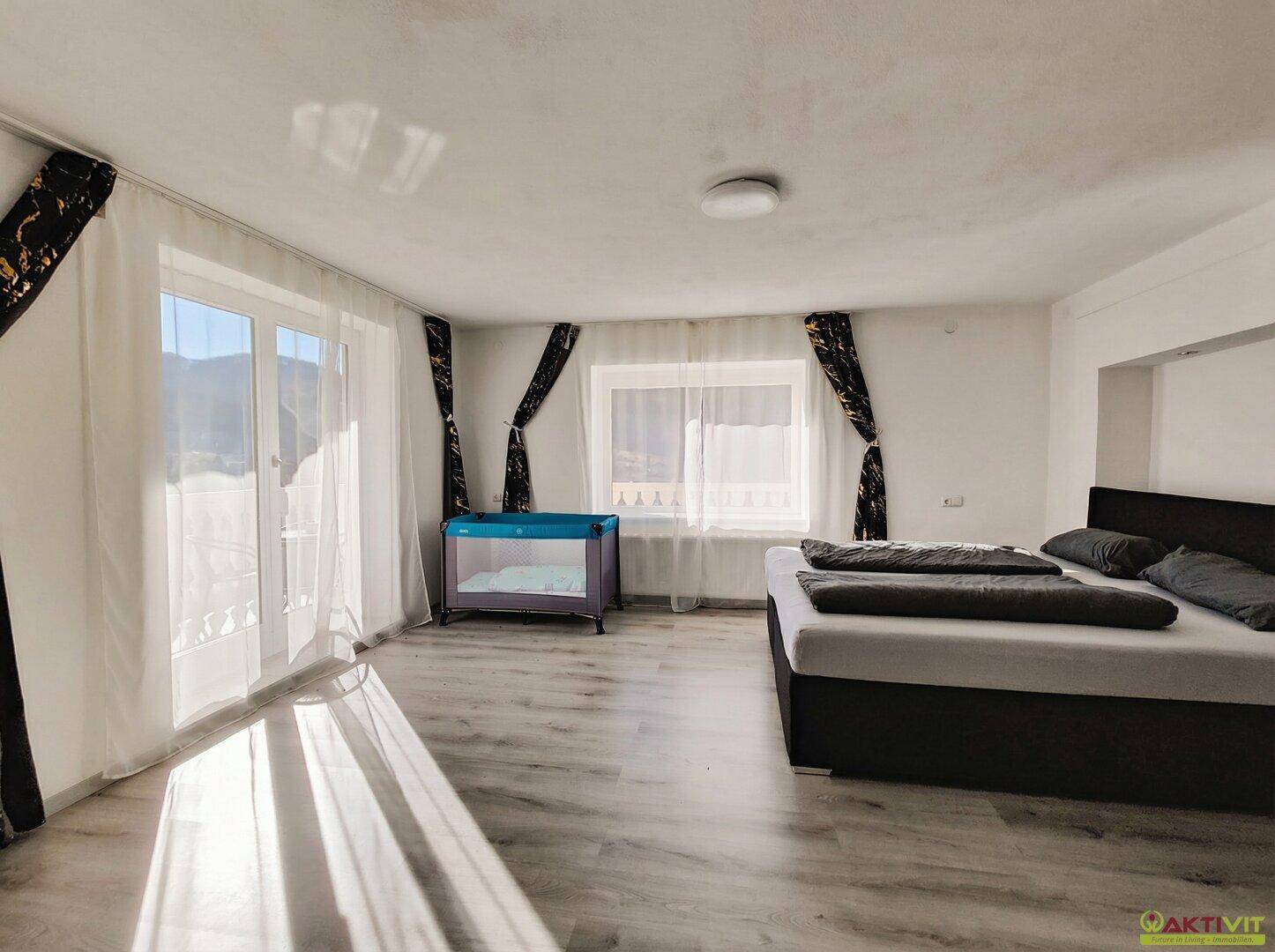 Helles Schlafzimmer mit Doppelbett, Kinderbett und Balkonzugang.