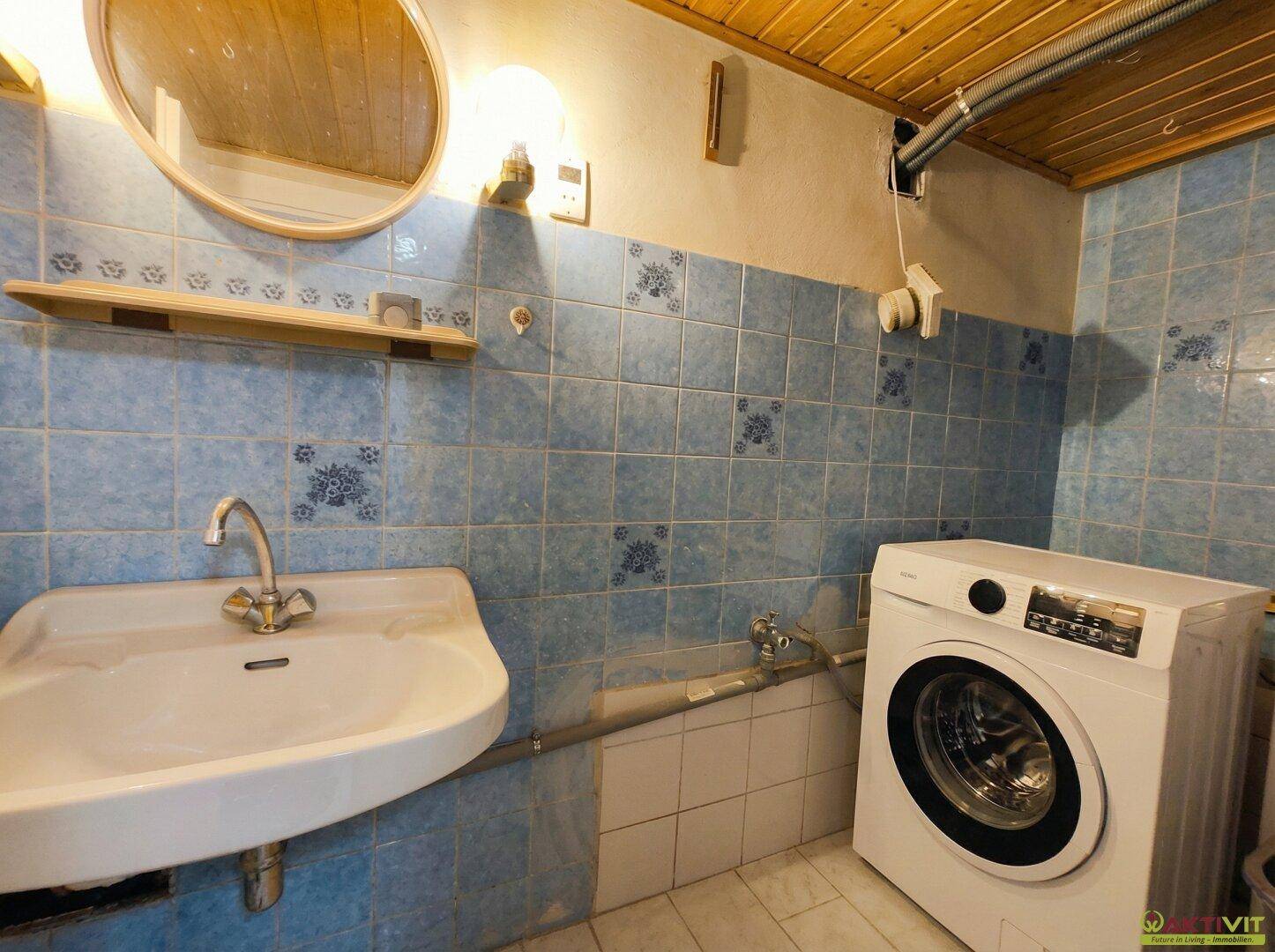 Funktionales Badezimmer mit Waschbecken, blauen Fliesen und Holzdecke, inklusive Waschmaschine.