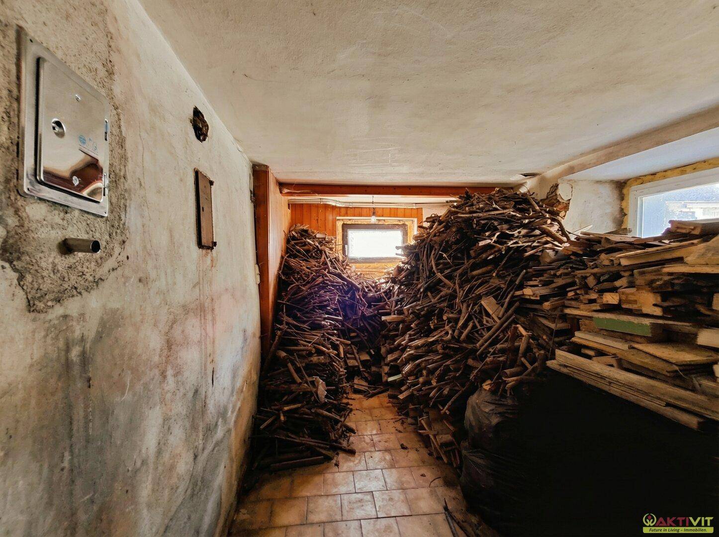 Geräumiger Lagerraum im Keller mit großen Mengen Brennholz und gefliestem Boden.