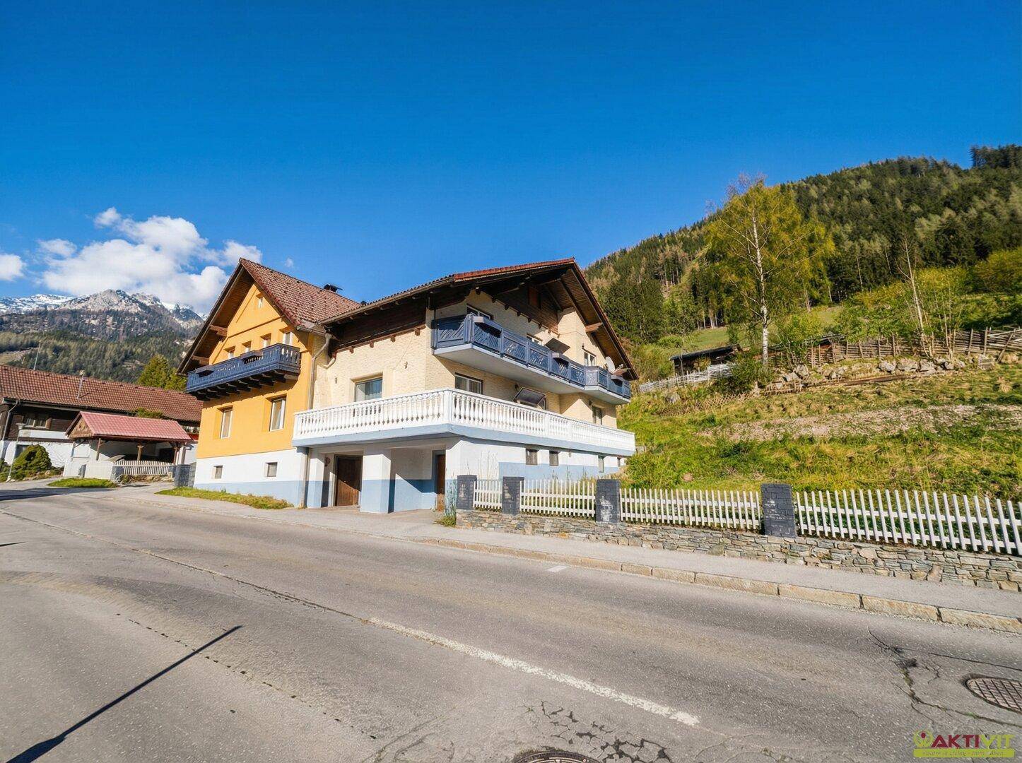 Wohnhaus mit Balkonen und Satteldach, gelegen an einer ruhigen Straße mit Bergblick.