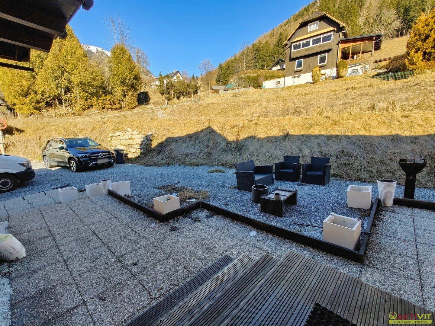 Gepflasterte Terrasse mit Sitzgelegenheiten und Blick auf die bewaldeten Hänge und Berge.