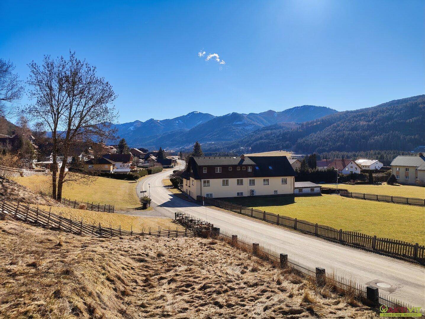 Weitläufiger Blick über die ländliche Umgebung mit Häusern und Bergen im Hintergrund.