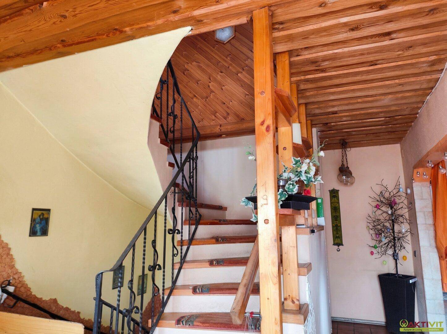 Holztreppe mit schmiedeeisernem Geländer und Holzverkleidung an Wänden und Decke.