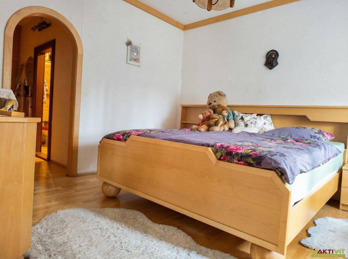 Helles Schlafzimmer mit hellem Holzbett, Parkettboden und Zugang zu einem Flur.