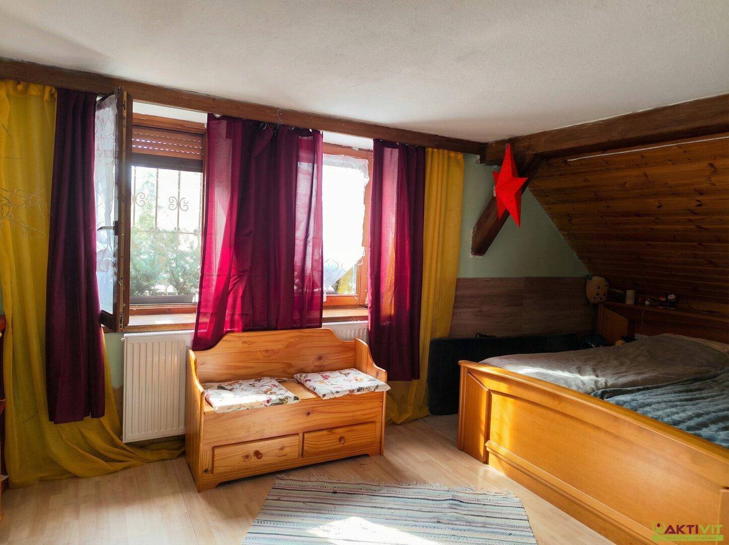 Dachgeschoss-Schlafzimmer mit Holzbalken, Fenster und rustikalem Holzbett.