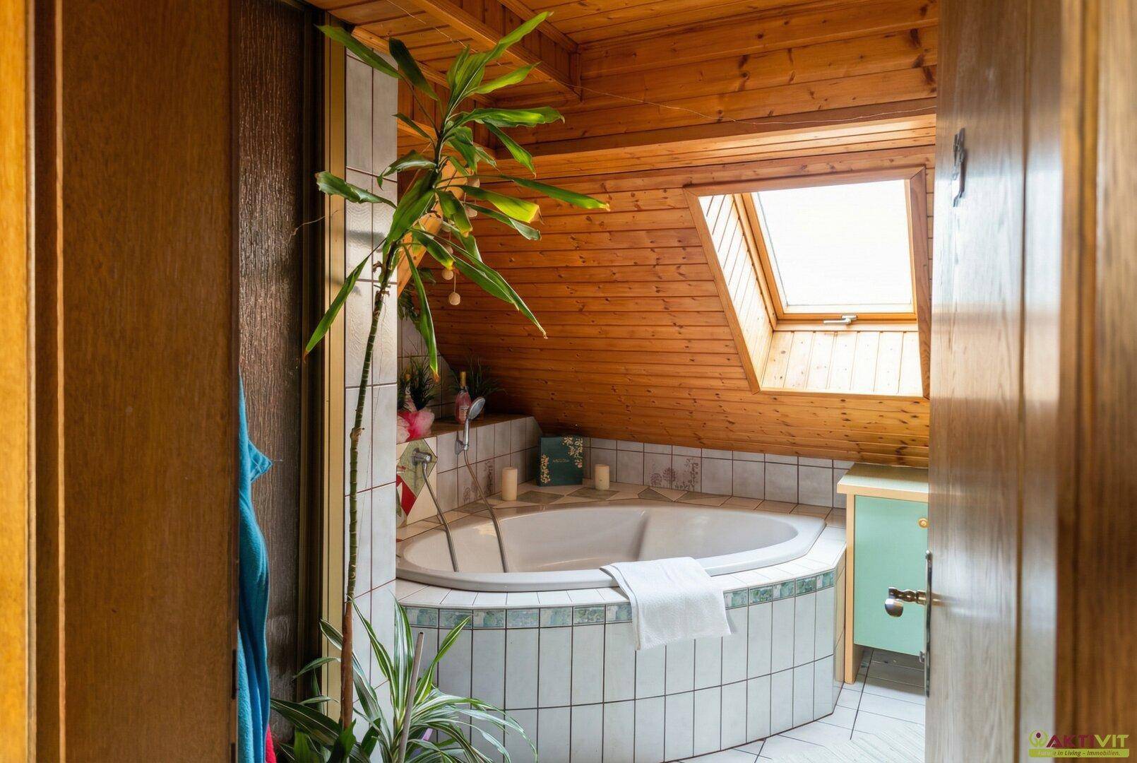 Badezimmer mit Eckbadewanne, Holzverkleidung und Dachfenster für natürliches Licht.
