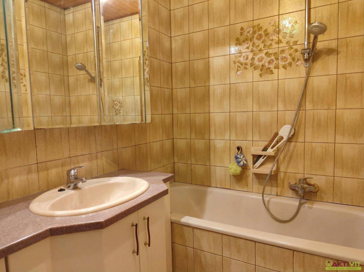 Badezimmer mit Badewanne, Waschbecken und Spiegelschrank in beigen Fliesen.