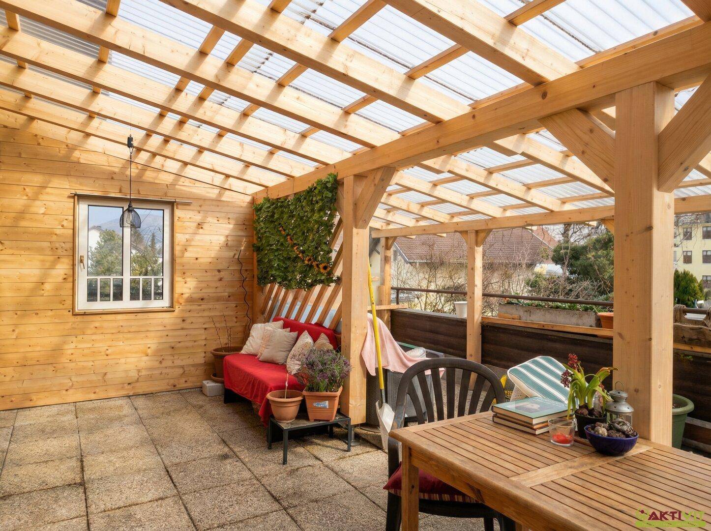Überdachte Terrasse mit Holzboden, Sitzgelegenheiten und Blick ins Grüne.