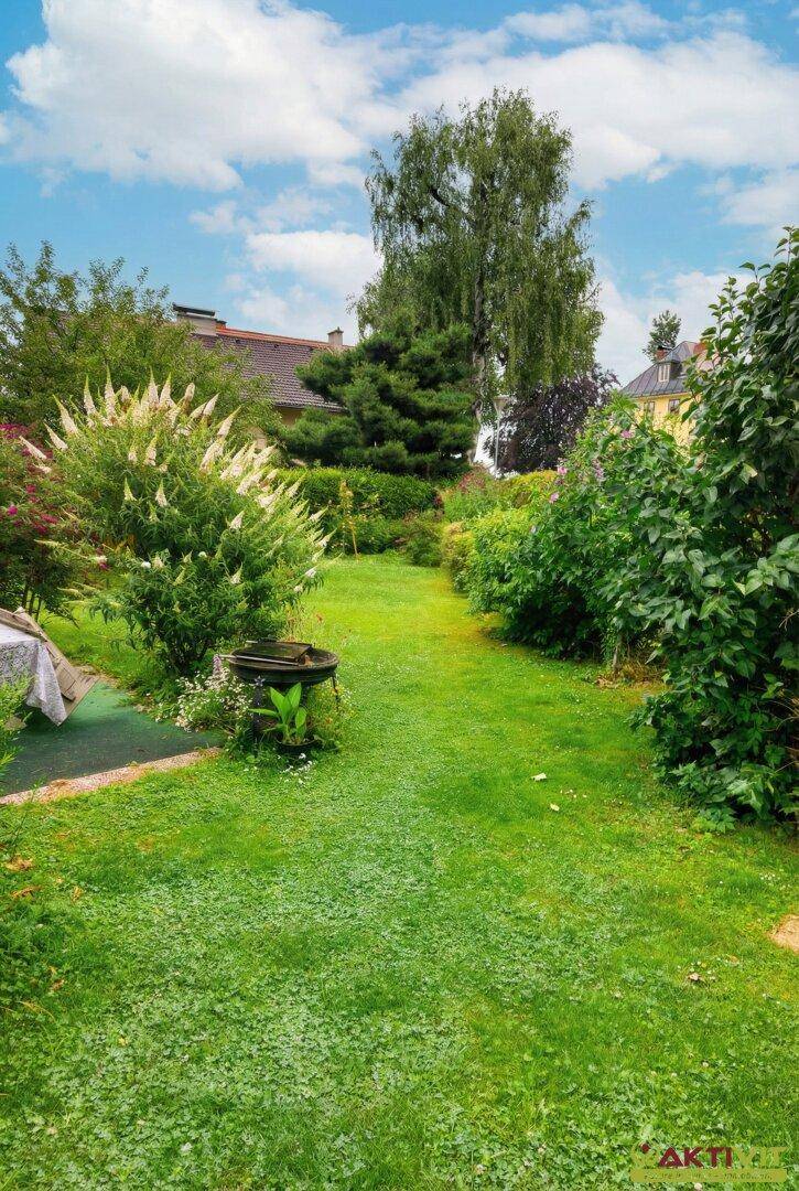 Gepflegter Garten mit Rasenfläche, Sträuchern und hohen Bäumen.