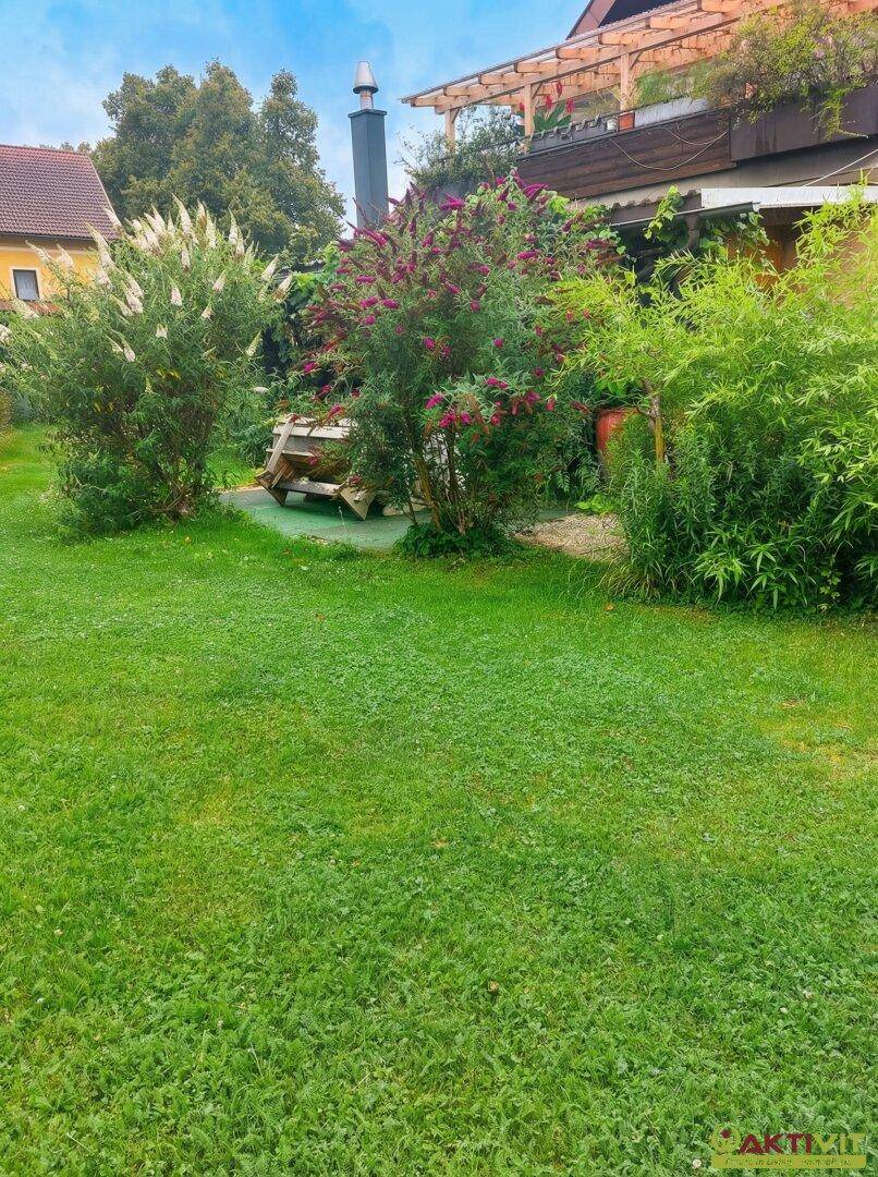 Großer Garten mit Rasen, blühenden Sträuchern und Blick auf das Haus.