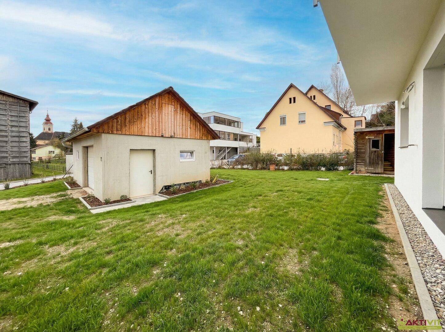 Grüner Gartenbereich mit Rasenfläche und einem Nebengebäude, umgeben von weiteren Häusern.