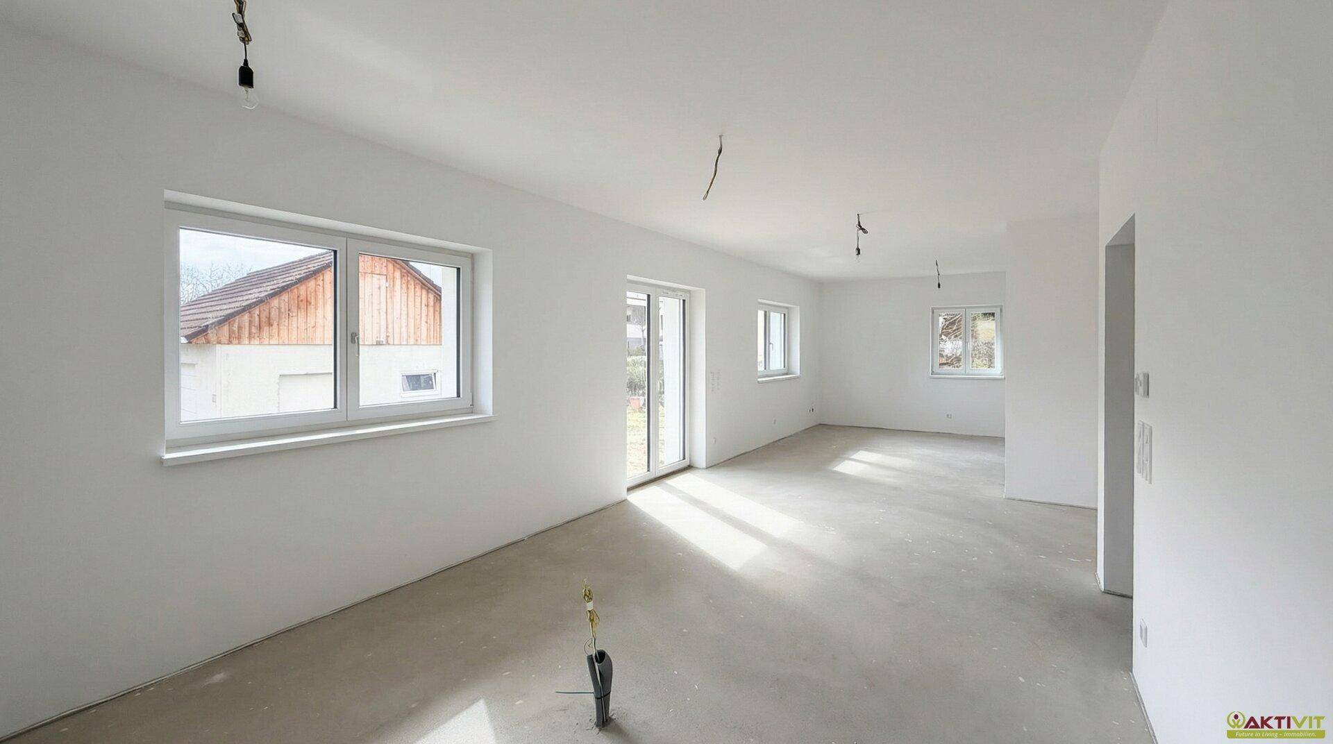Geräumiges Wohnzimmer im Rohbau mit großen Fenstern und Zugang zur Terrasse, viel Tageslicht.