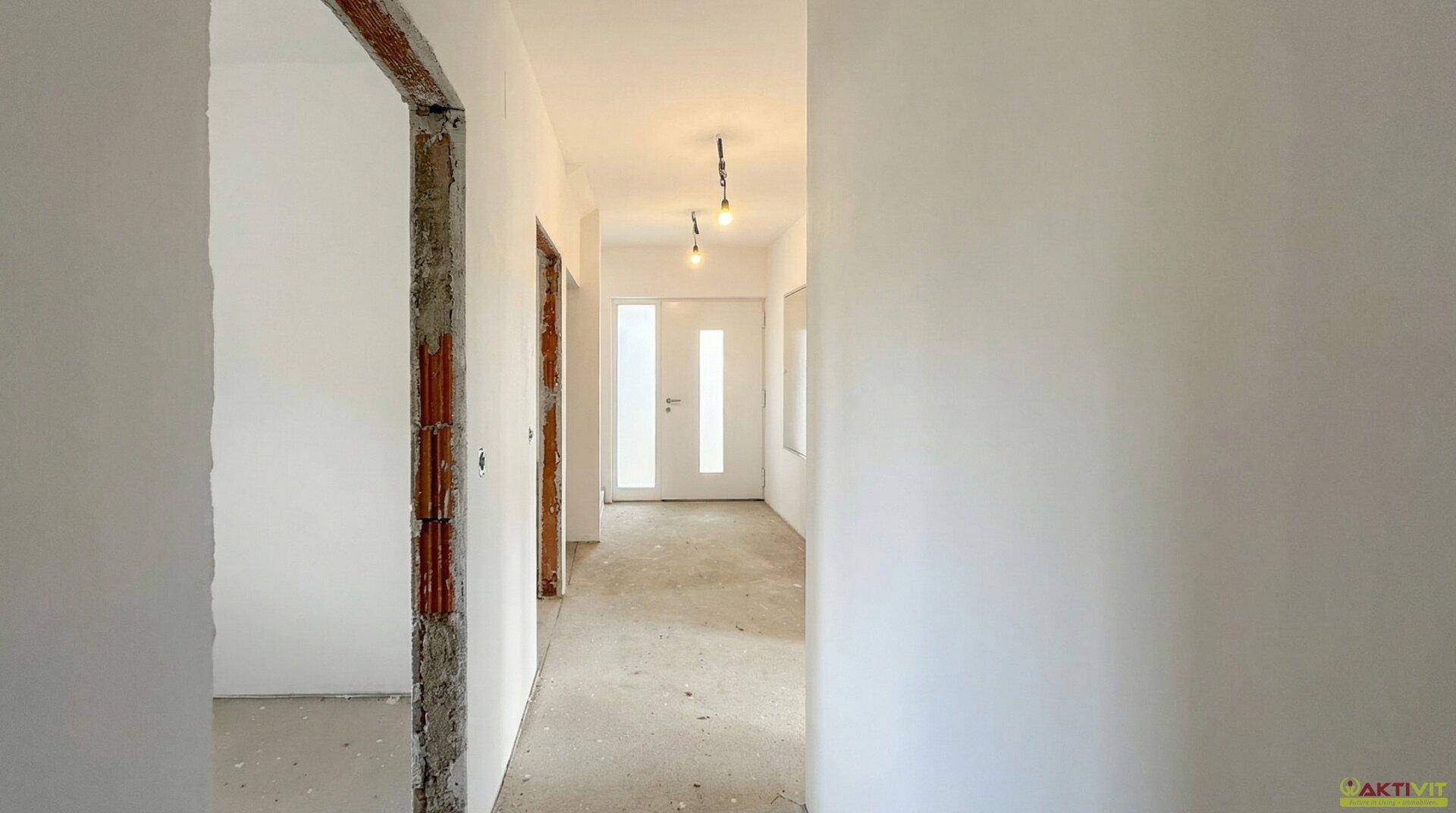 Unfertiger Flur mit Rohbauwänden und provisorischer Beleuchtung, bereit für den Ausbau.