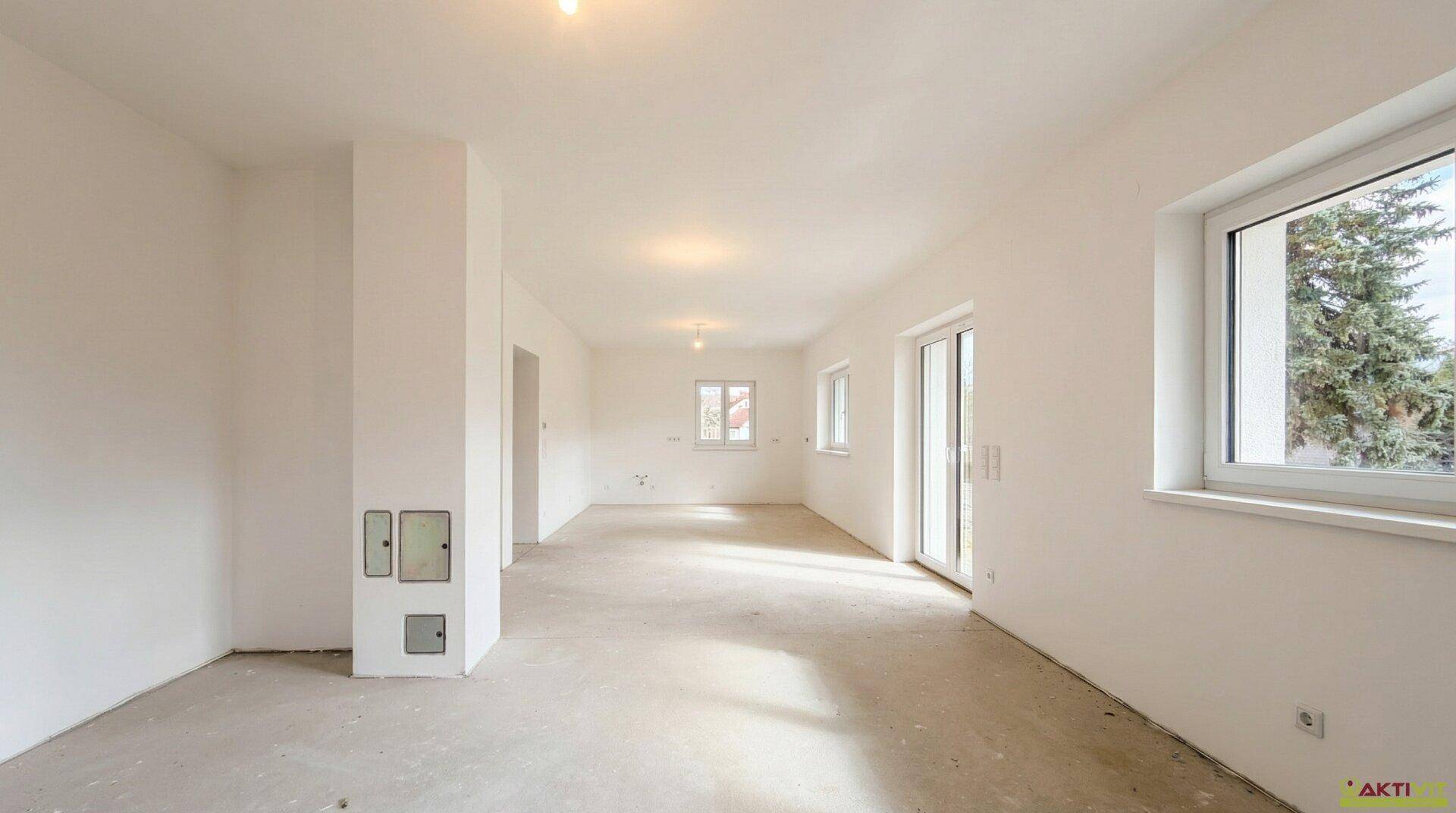 Großzügiger Wohnraum im Rohbau mit Fenstern und Terrassentür, bietet viel Gestaltungspotenzial.