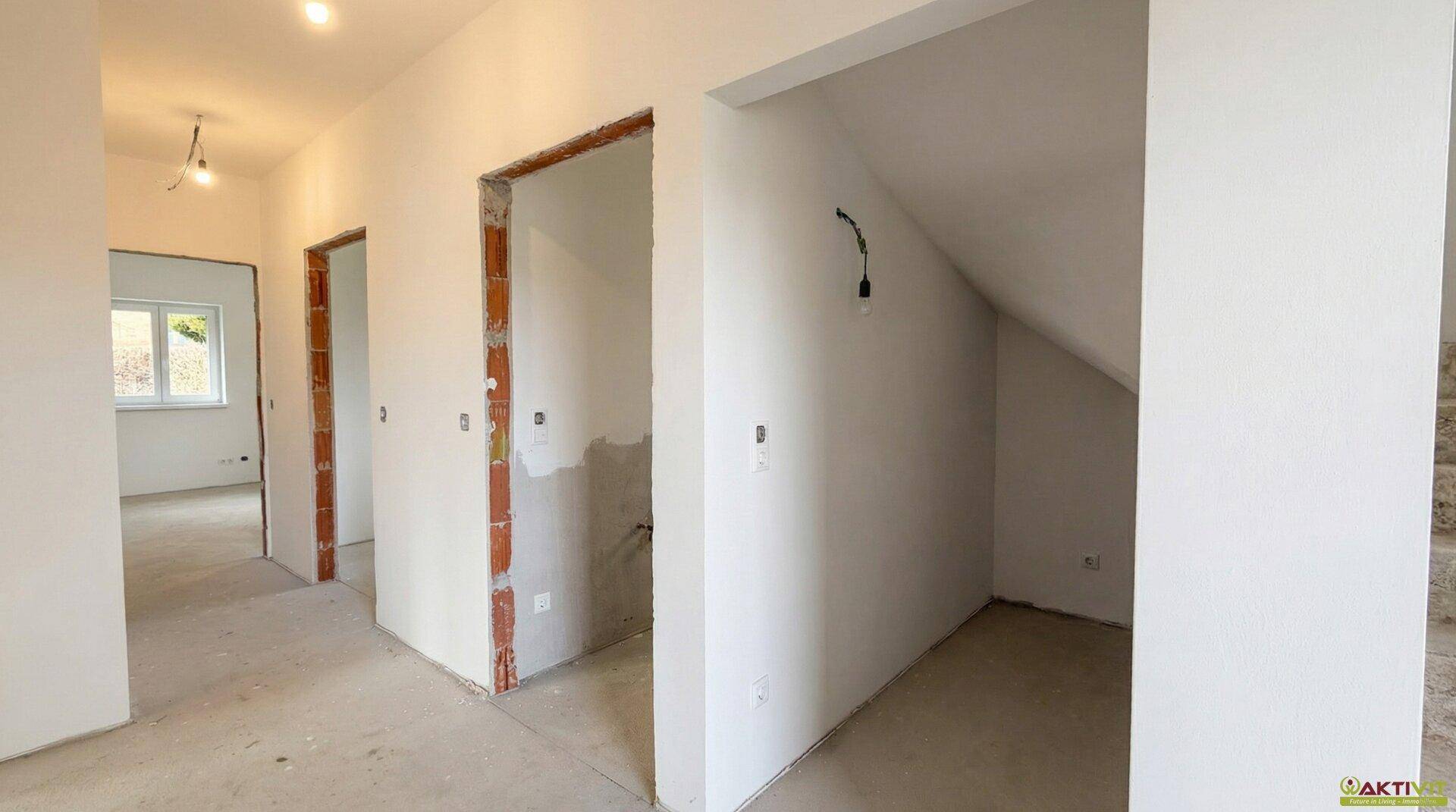 Flurbereich im Rohbau mit vorbereiteten Türöffnungen und Nische unter der Treppe.