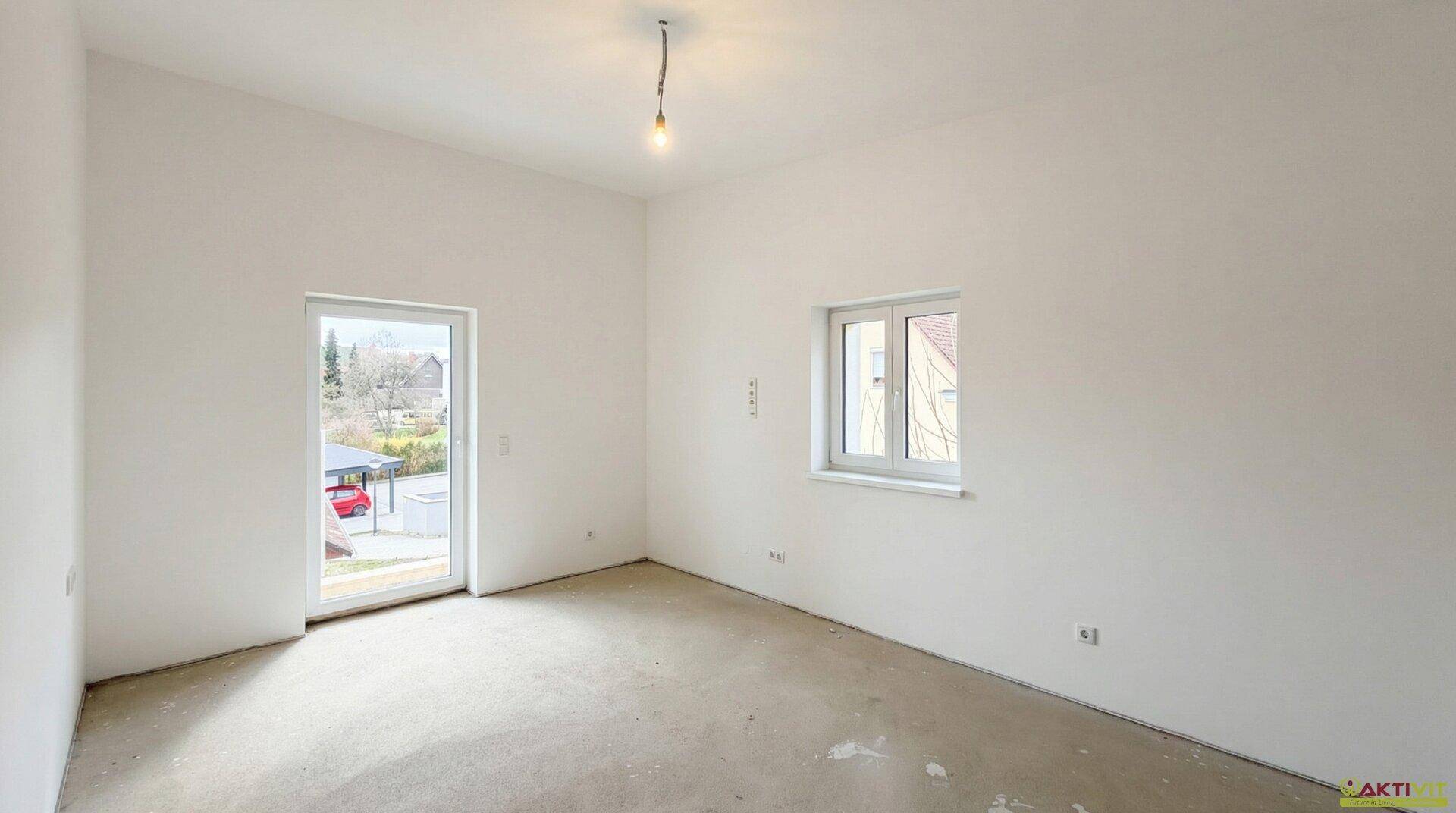 Geräumiger Raum im Rohbau mit Fenstertür und zusätzlichem Fenster, viel Tageslicht.