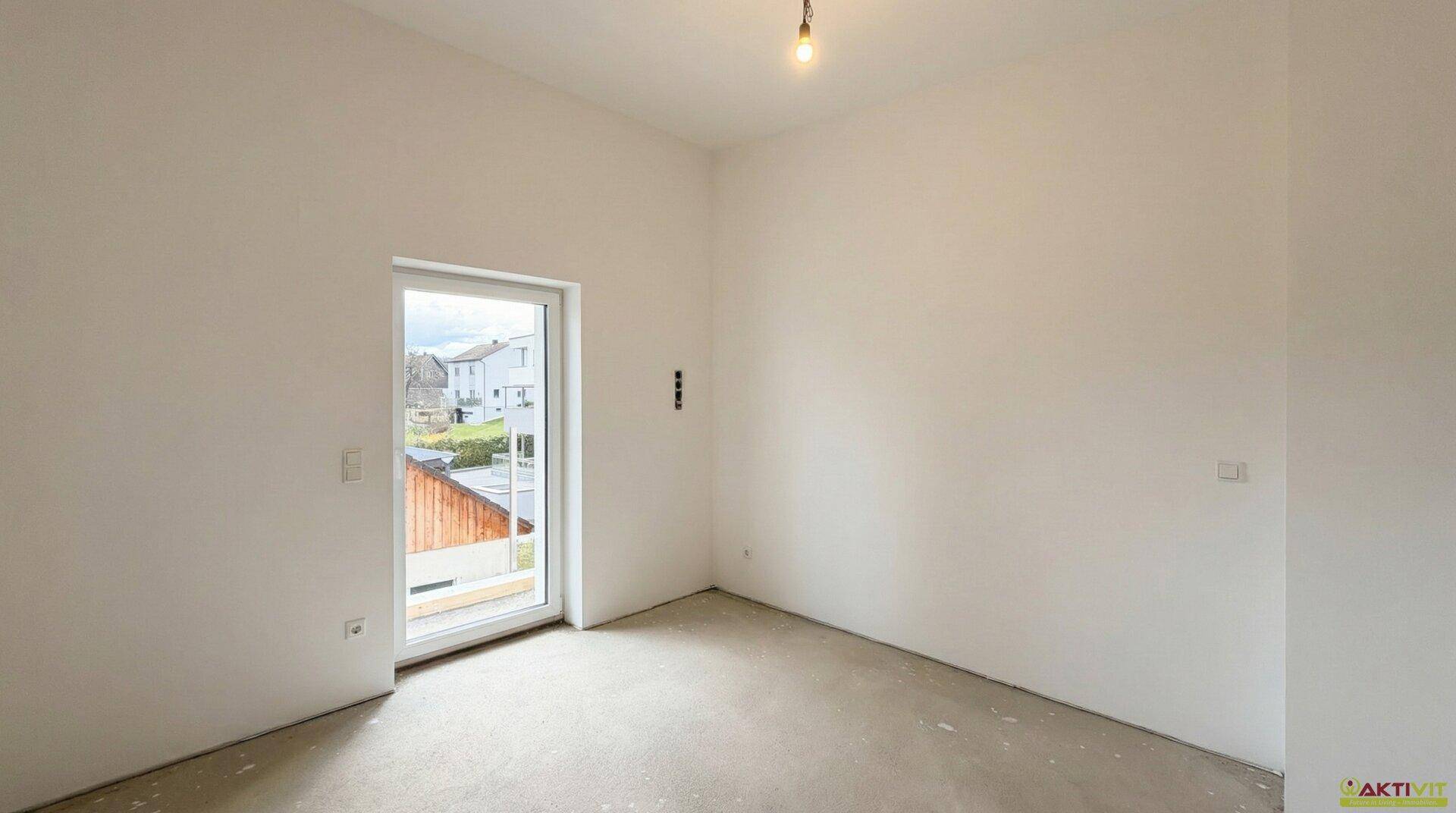 Heller Raum im Rohbau mit Fenstertür, die Zugang zu einem Balkon oder einer Terrasse bietet.