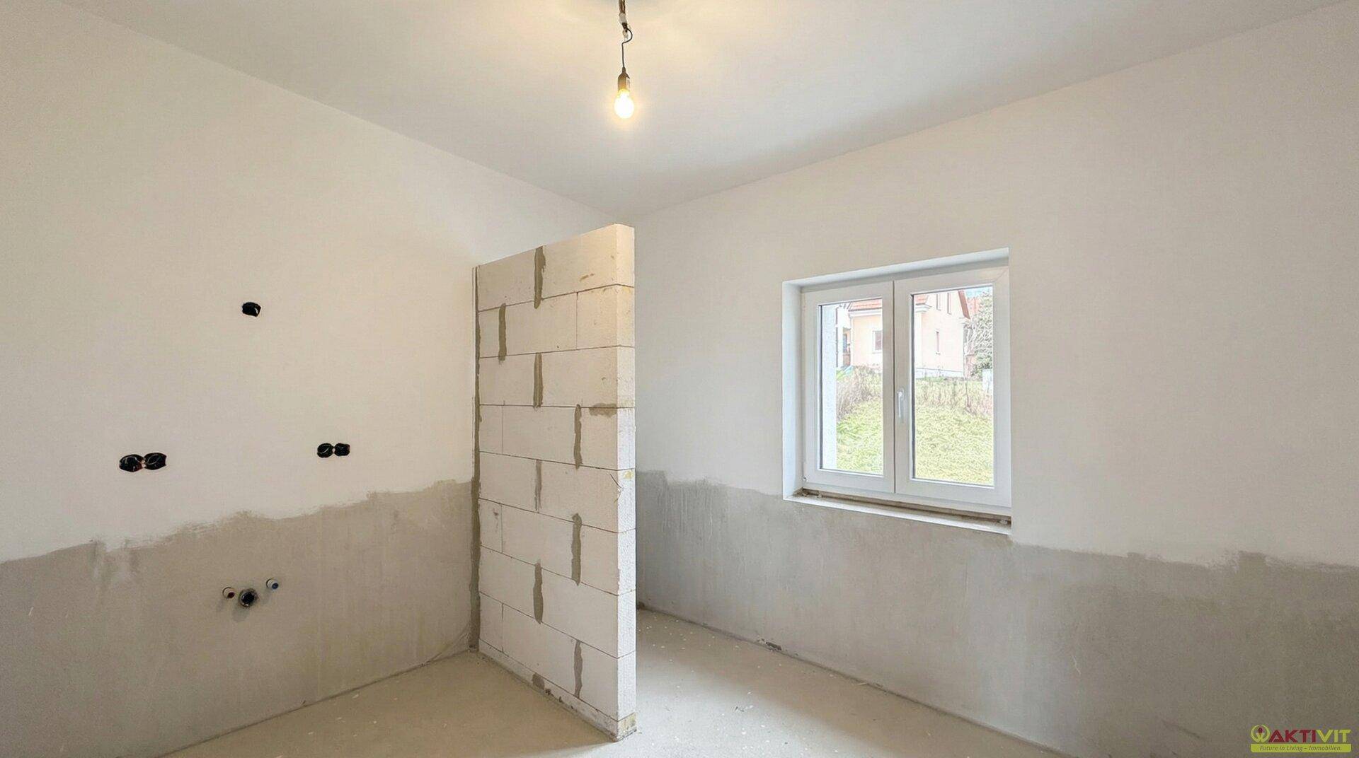 Badezimmer im Rohbau mit vorbereiteten Anschlüssen und einer Trennwand, bereit für den Ausbau.