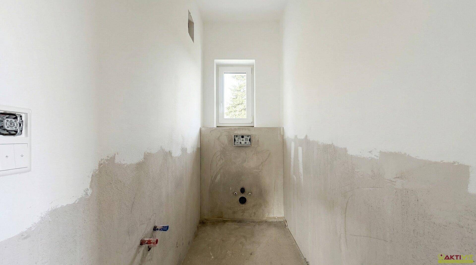 Kleines WC oder Gästebad im Rohbau mit Fenster und vorbereiteten Sanitäranschlüssen.