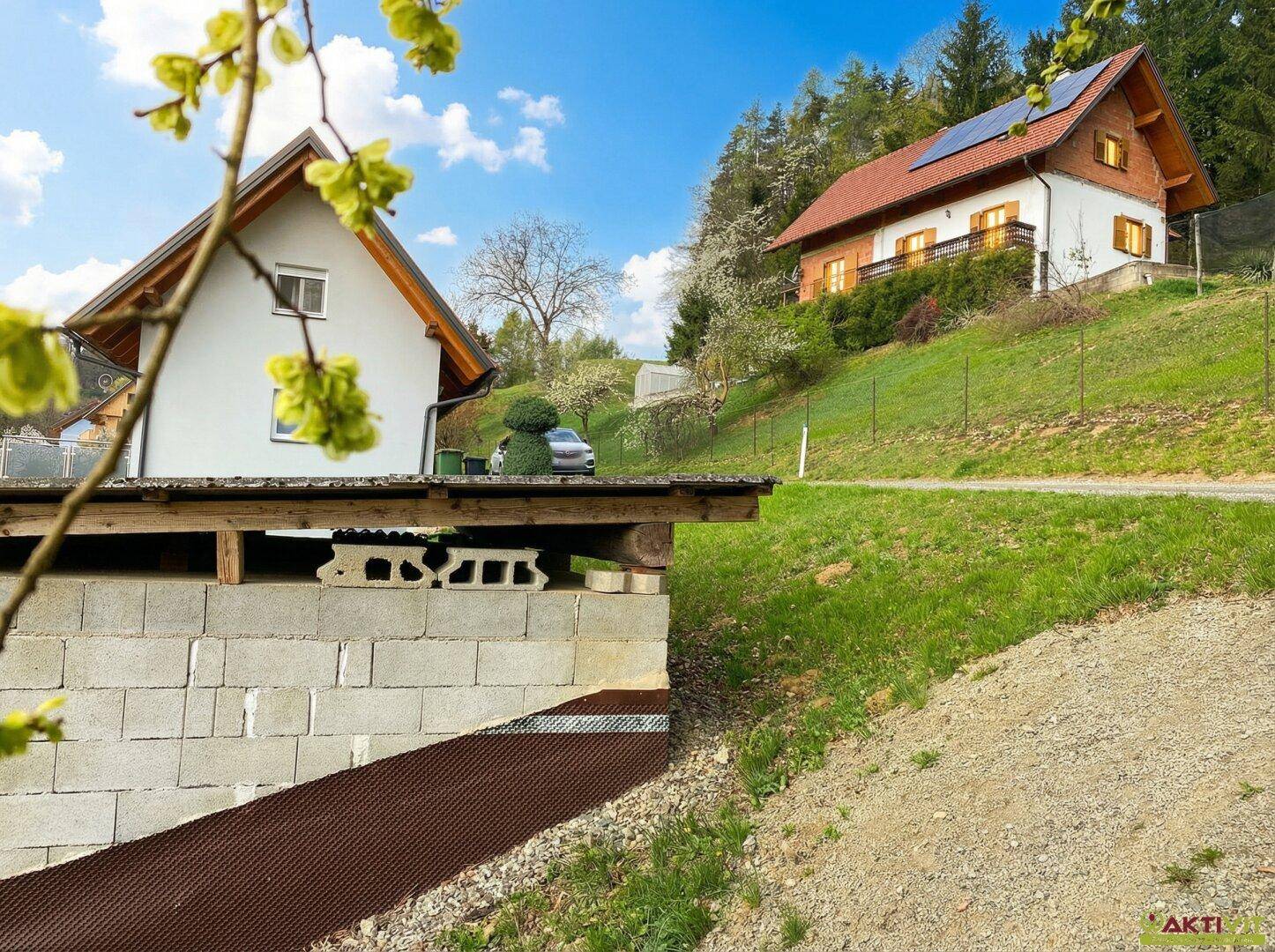 Zwei Häuser auf einem grünen Hang mit Solarpaneelen auf dem Dach des oberen Gebäudes.