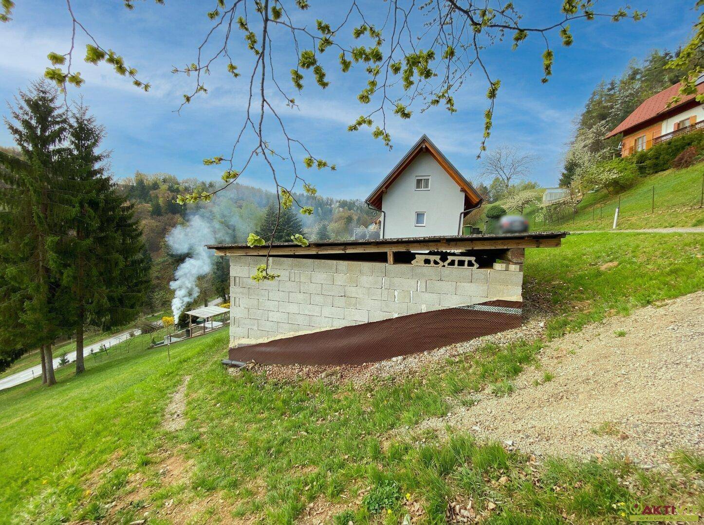 Zwei Häuser auf einem Hang, das untere Gebäude ist ein Rohbau aus Betonblöcken.