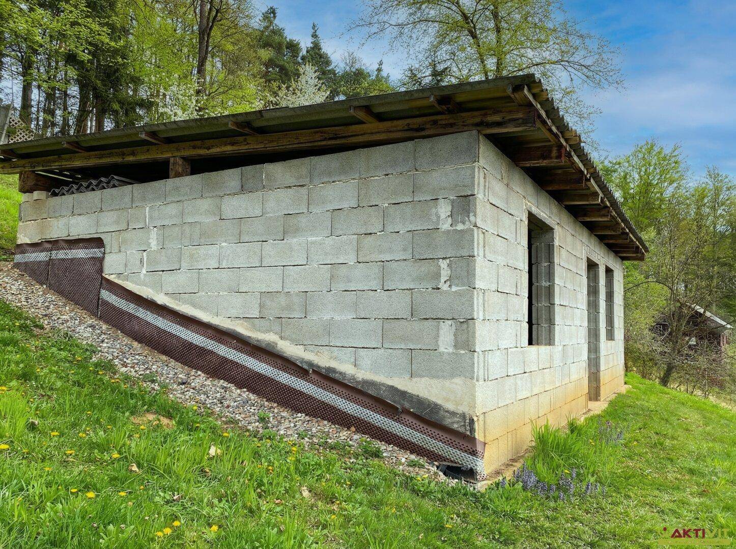 Unfertiges Gebäude aus Betonblöcken mit einfacher Dachkonstruktion auf einem grünen Hang.
