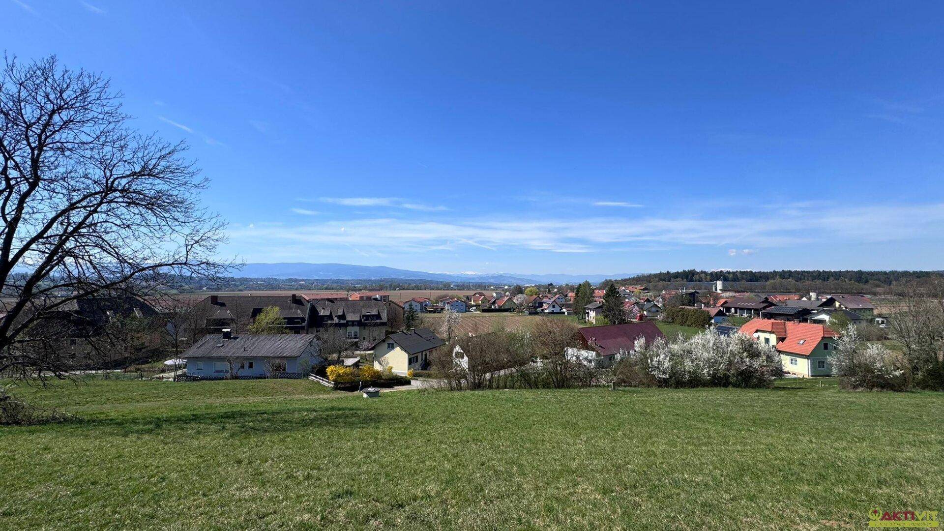 Panoramablick über eine ländliche Siedlung mit Bergen im Hintergrund und weitem Himmel.