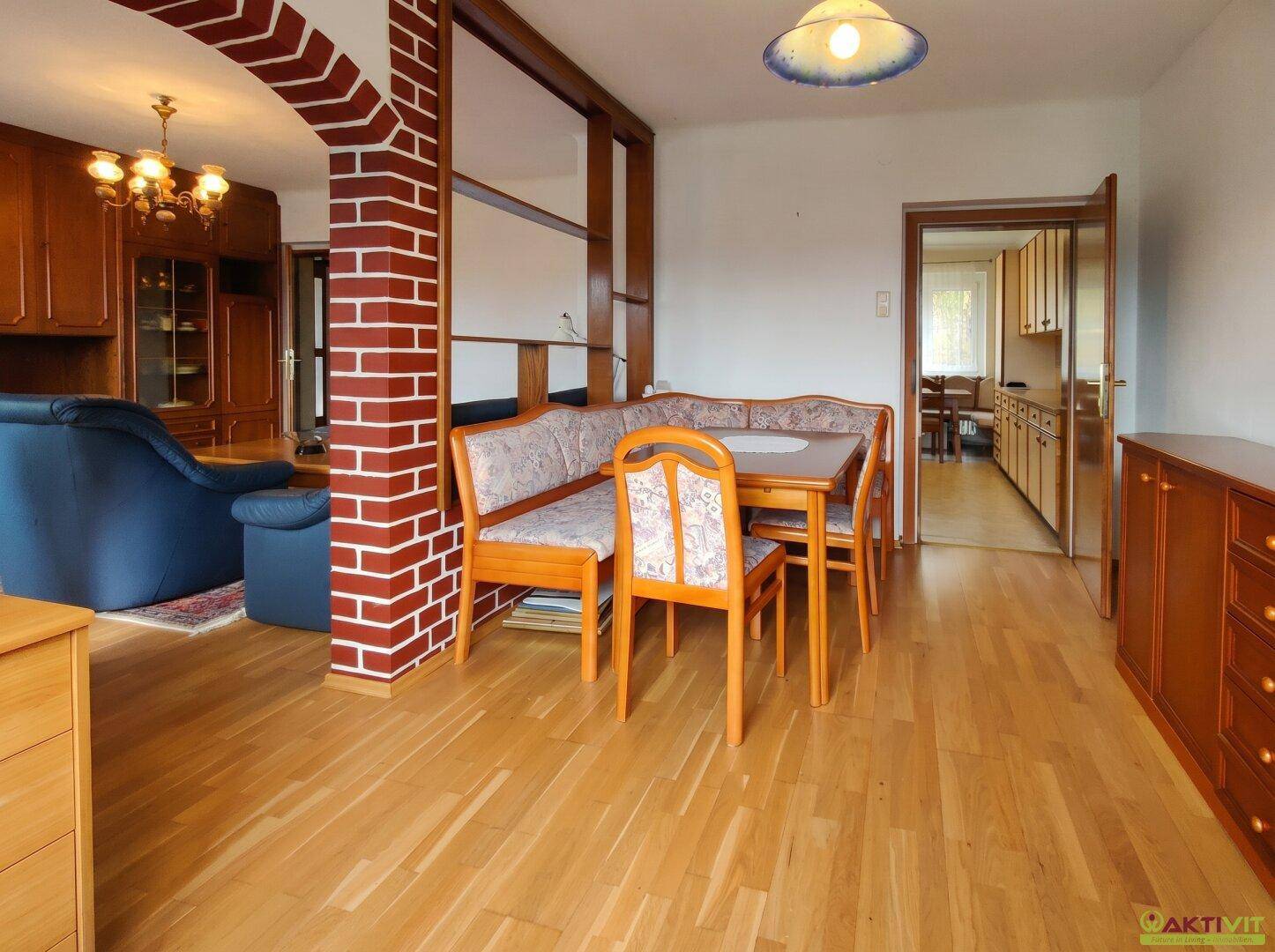 Gemütlicher Wohn-Essbereich mit Holzboden und traditionellen Möbeln, verbunden durch einen gemauerten Bogen.