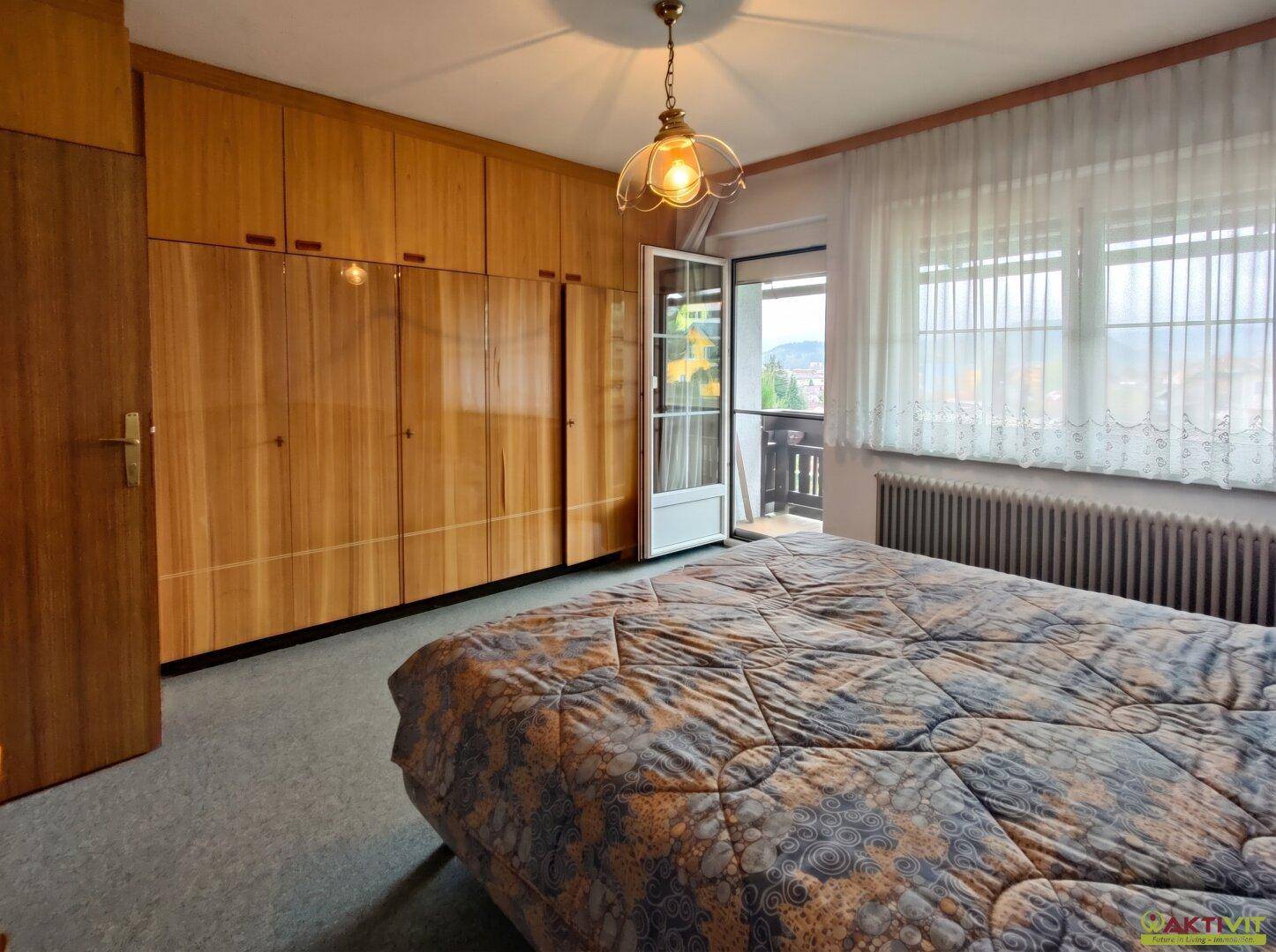 Schlafzimmer mit großem Bett, Holzschrank und Zugang zu einem Balkon mit Aussicht.