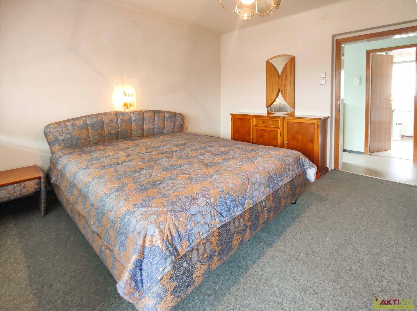 Schlafzimmer mit Doppelbett, Nachttisch und Kommode mit Spiegel.