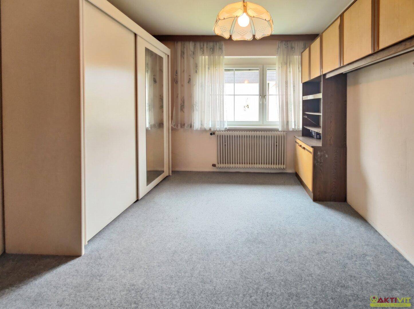 Helles Schlafzimmer mit Einbauschrank, Fenster und Teppichboden.
