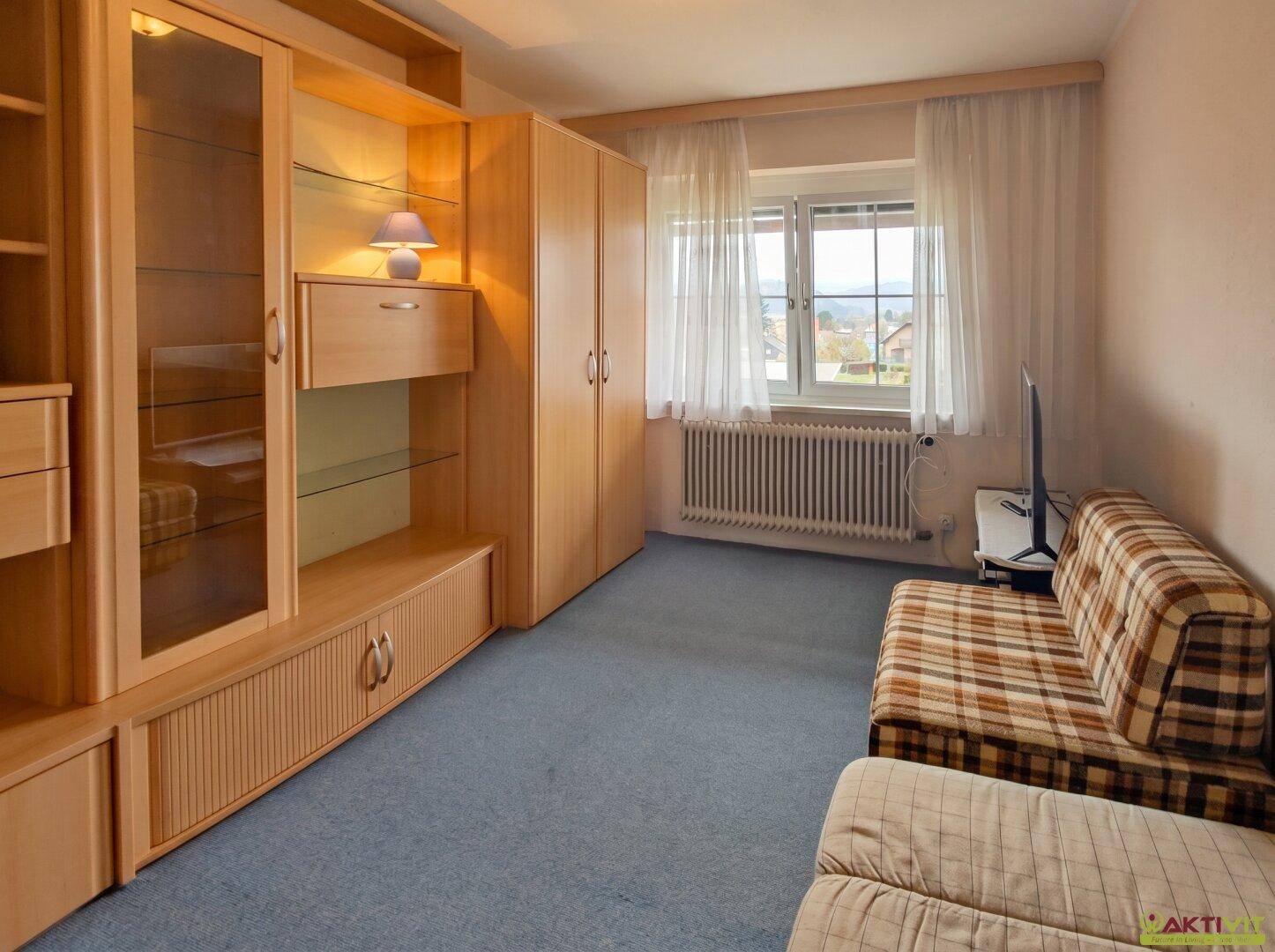 Zimmer mit Schlafsofa, Holzschrankwand und Fenster mit Blick ins Grüne.