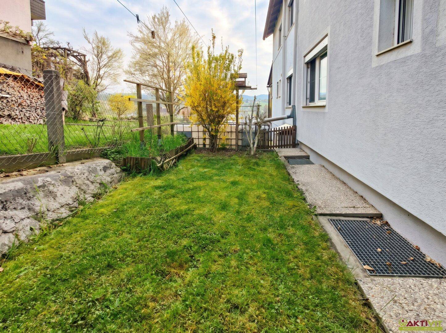 Kleiner Rasenbereich neben dem Haus mit einfacher Bepflanzung.