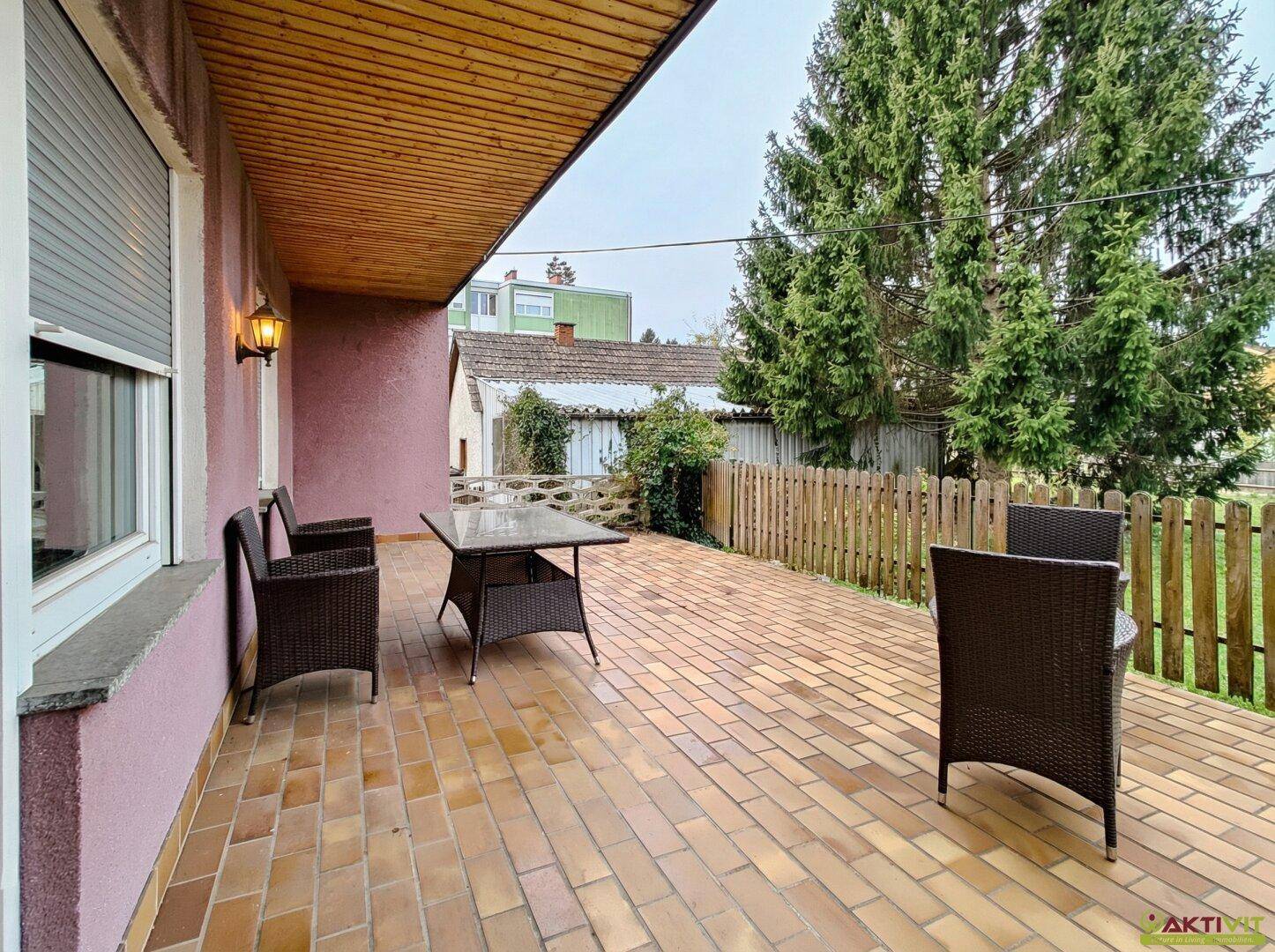 Geflieste Terrasse mit Sitzgelegenheiten und Blick in den Garten.