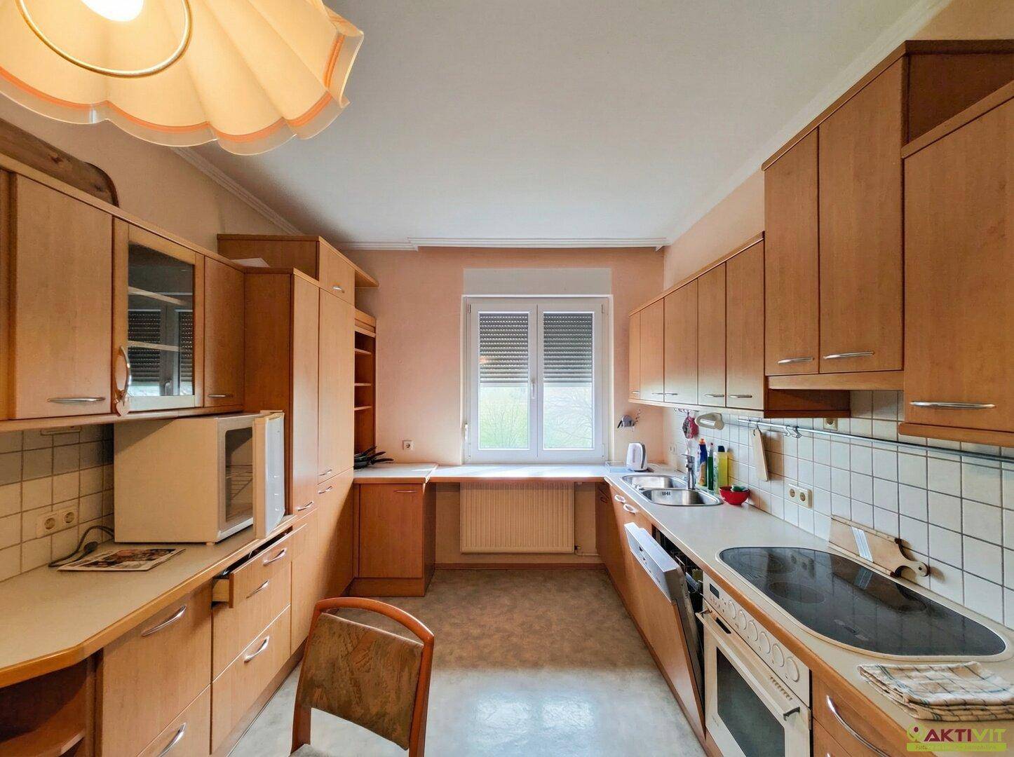 Küche mit hellen Holzschränken, Fenster und grundlegenden Küchengeräten.