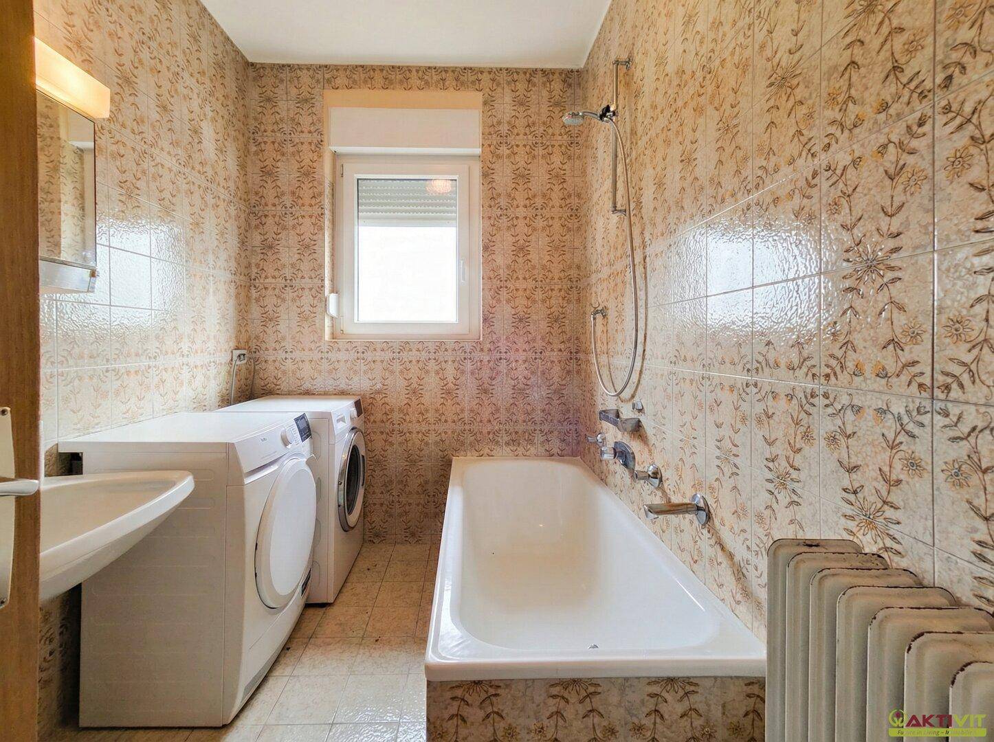 Badezimmer mit gemusterten Fliesen, Badewanne und Waschmaschine.