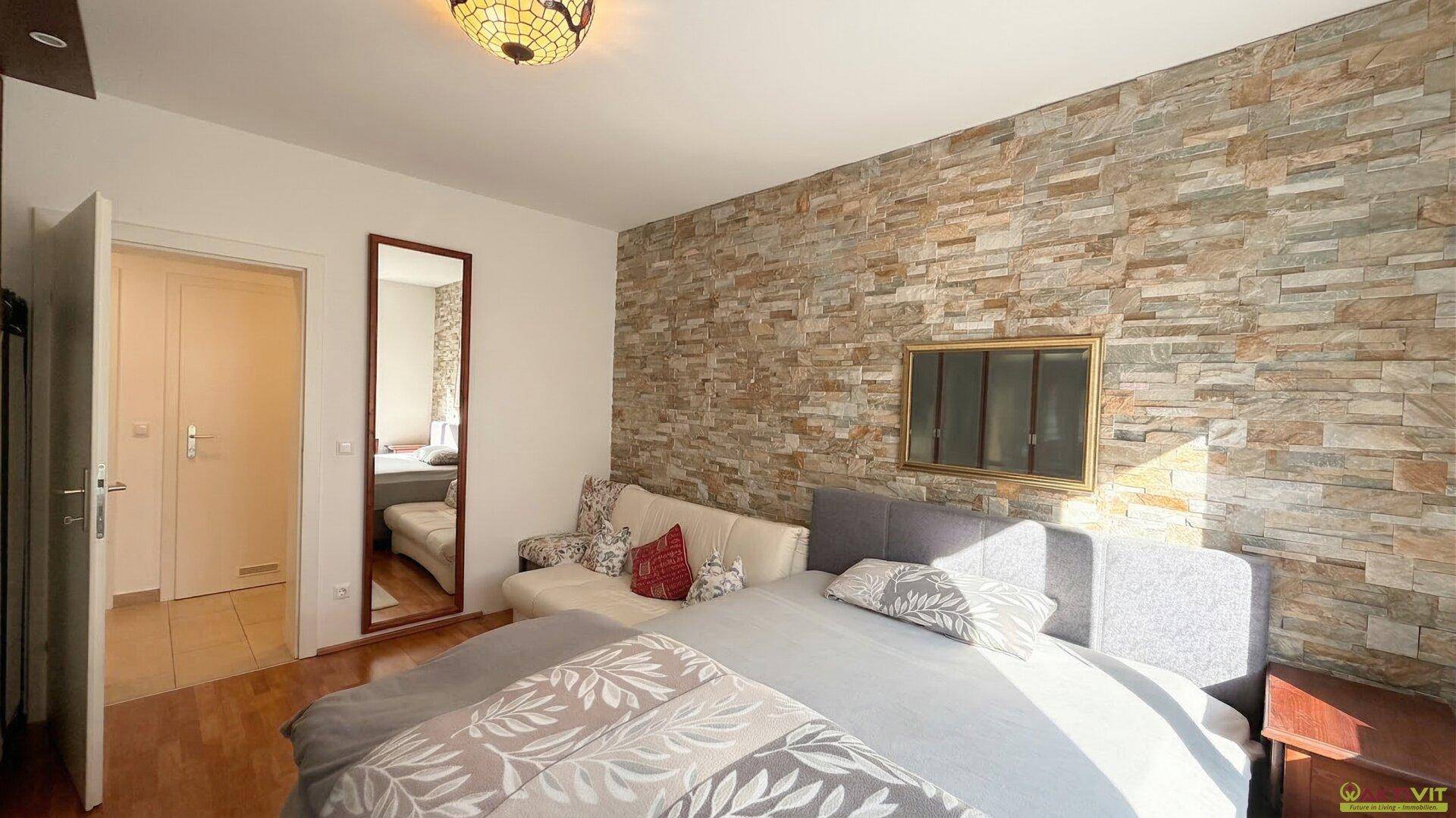 Schlafzimmer mit Steinwand, Doppelbett und Holzboden, hell beleuchtet.