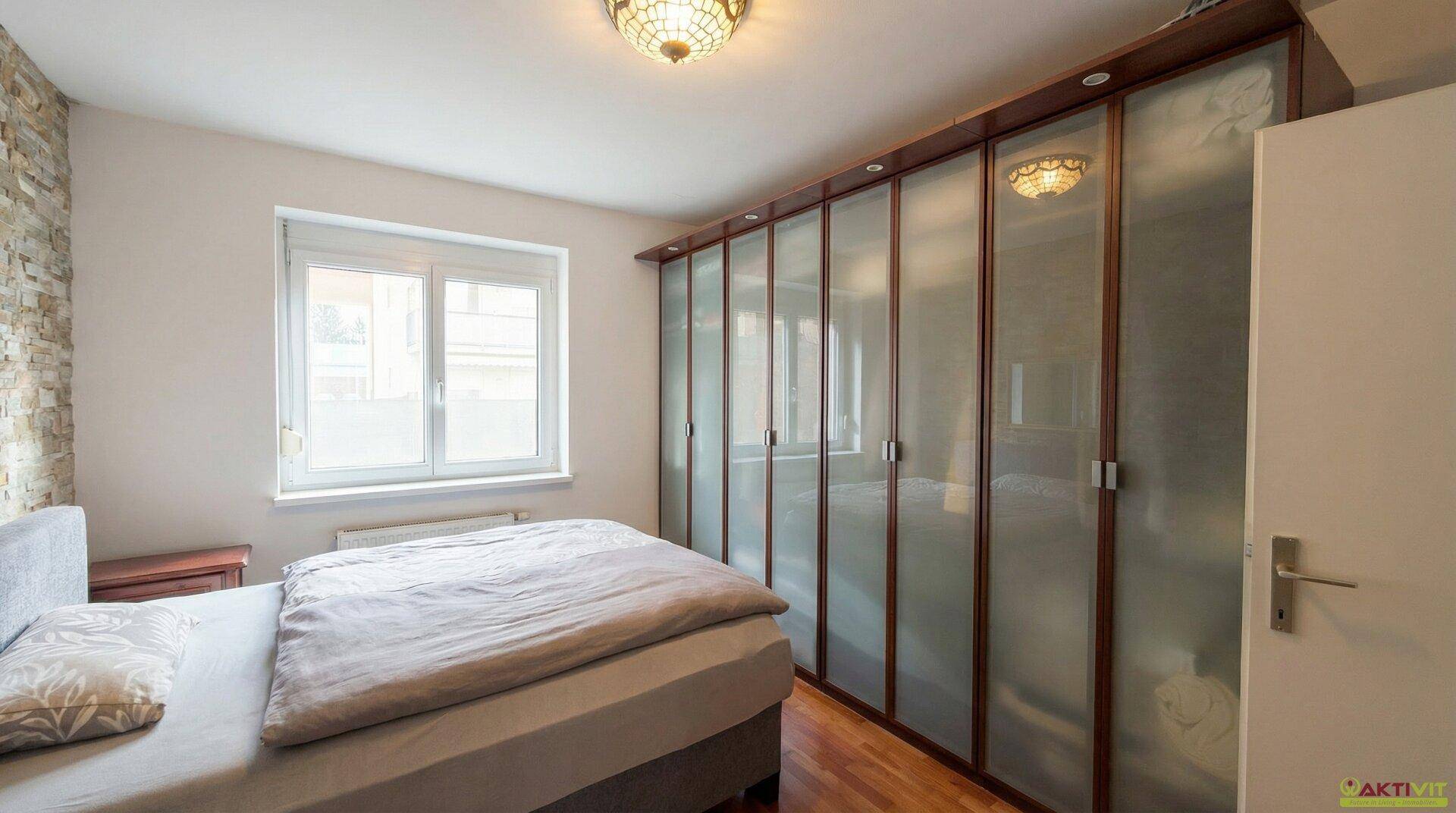 Schlafzimmer mit großem Einbauschrank, Doppelbett und Fenster mit viel Tageslicht.