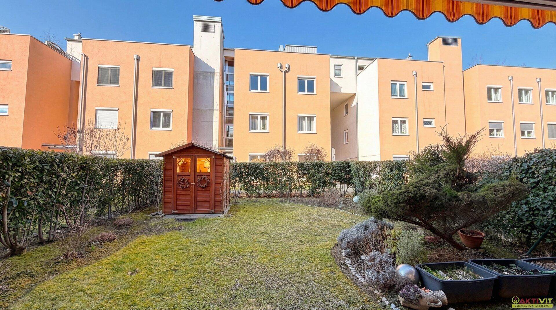 Gepflegter Gartenbereich mit Rasen, Hecke und Gartenhaus hinter dem Wohngebäude.