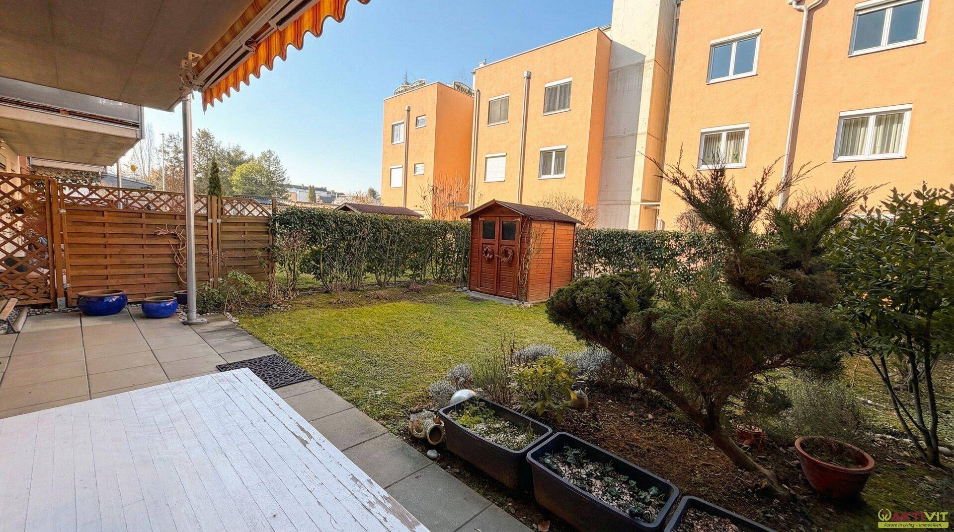 Sonniger Garten mit Terrasse, Rasenfläche und Blick auf die umliegenden Gebäude.