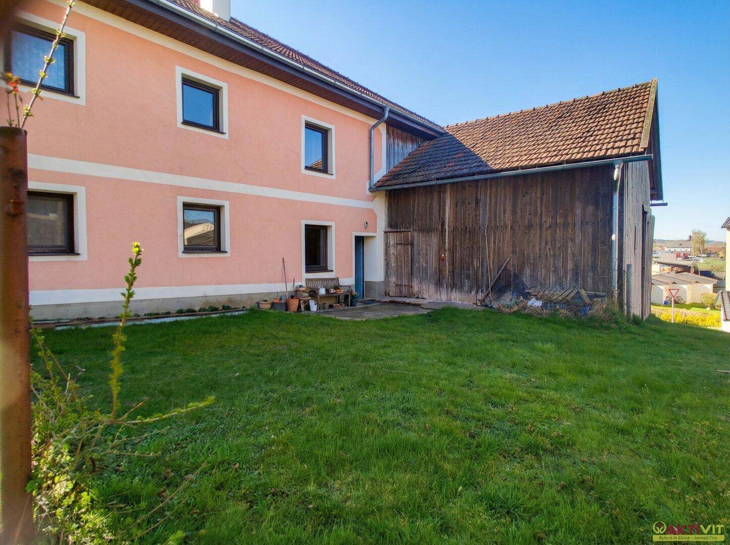 Seitenansicht des Wohnhauses mit angrenzendem Holzschuppen und gepflegtem Rasenbereich.