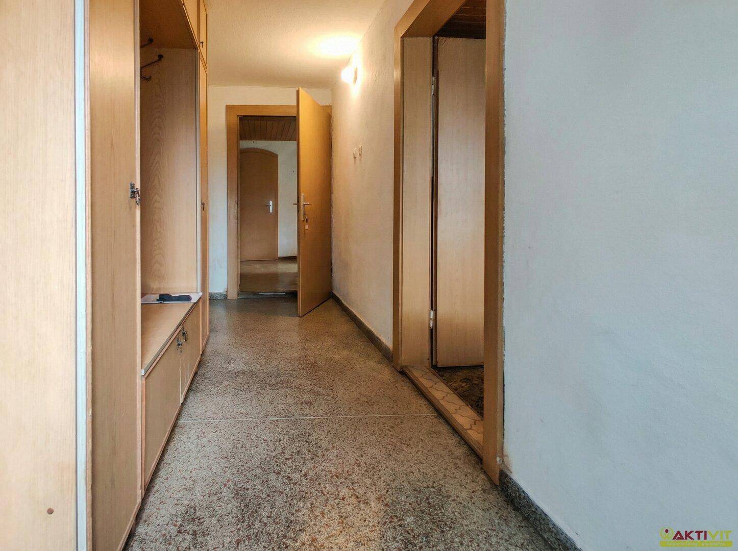 Langer Flur mit Einbauschränken, Terrazzoboden und Holztüren.