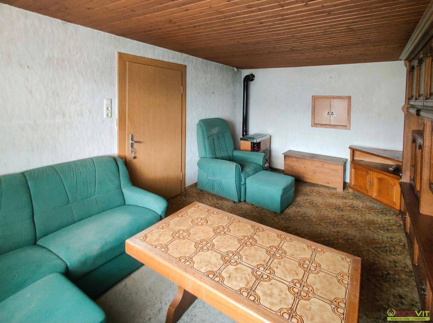 Gemütliches Wohnzimmer mit Holzdecke, Kaminofen und Teppichboden in Grün.