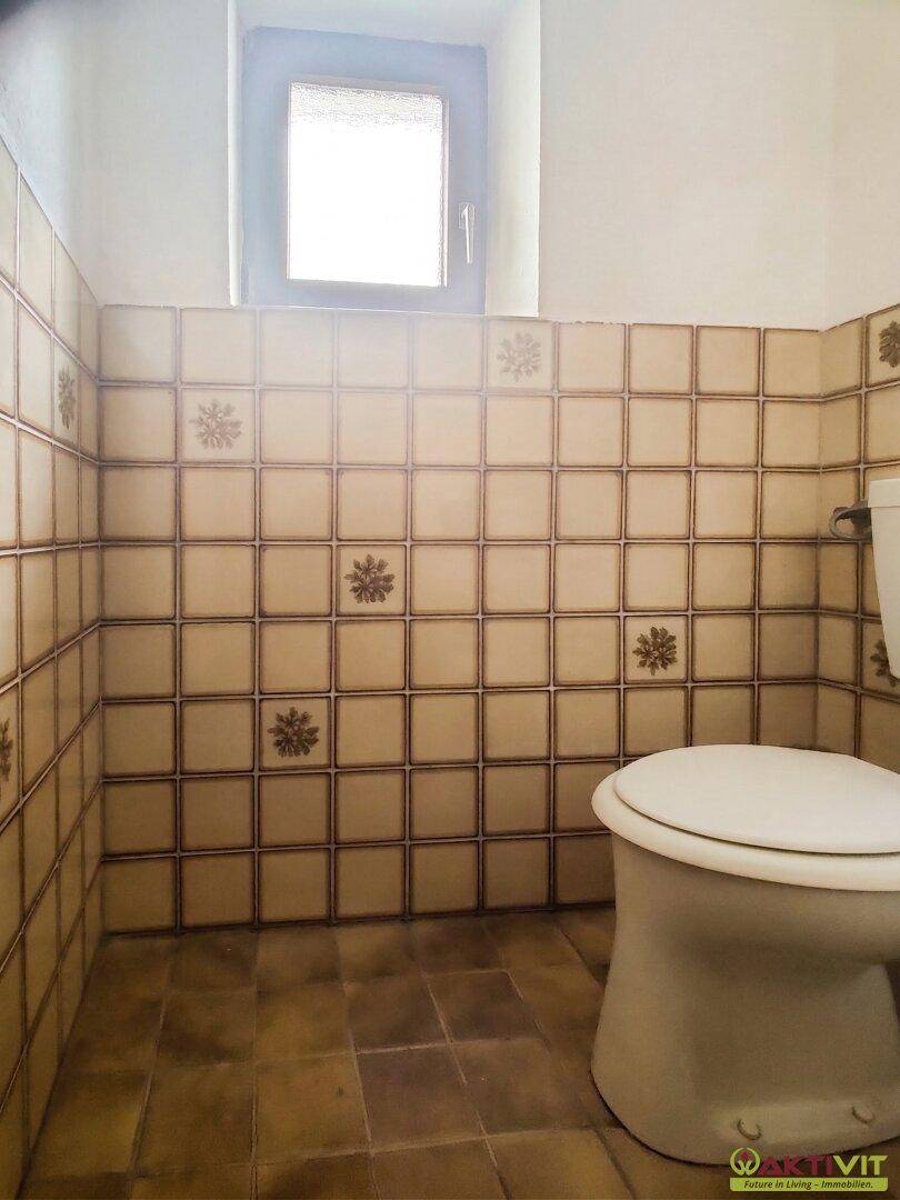 Separate Toilette mit gemusterten Fliesen und kleinem Fenster.