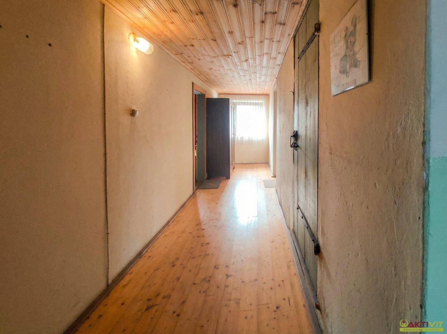 Langer Flur mit Holzdielenboden, Holzdecke und natürlichem Lichteinfall am Ende.